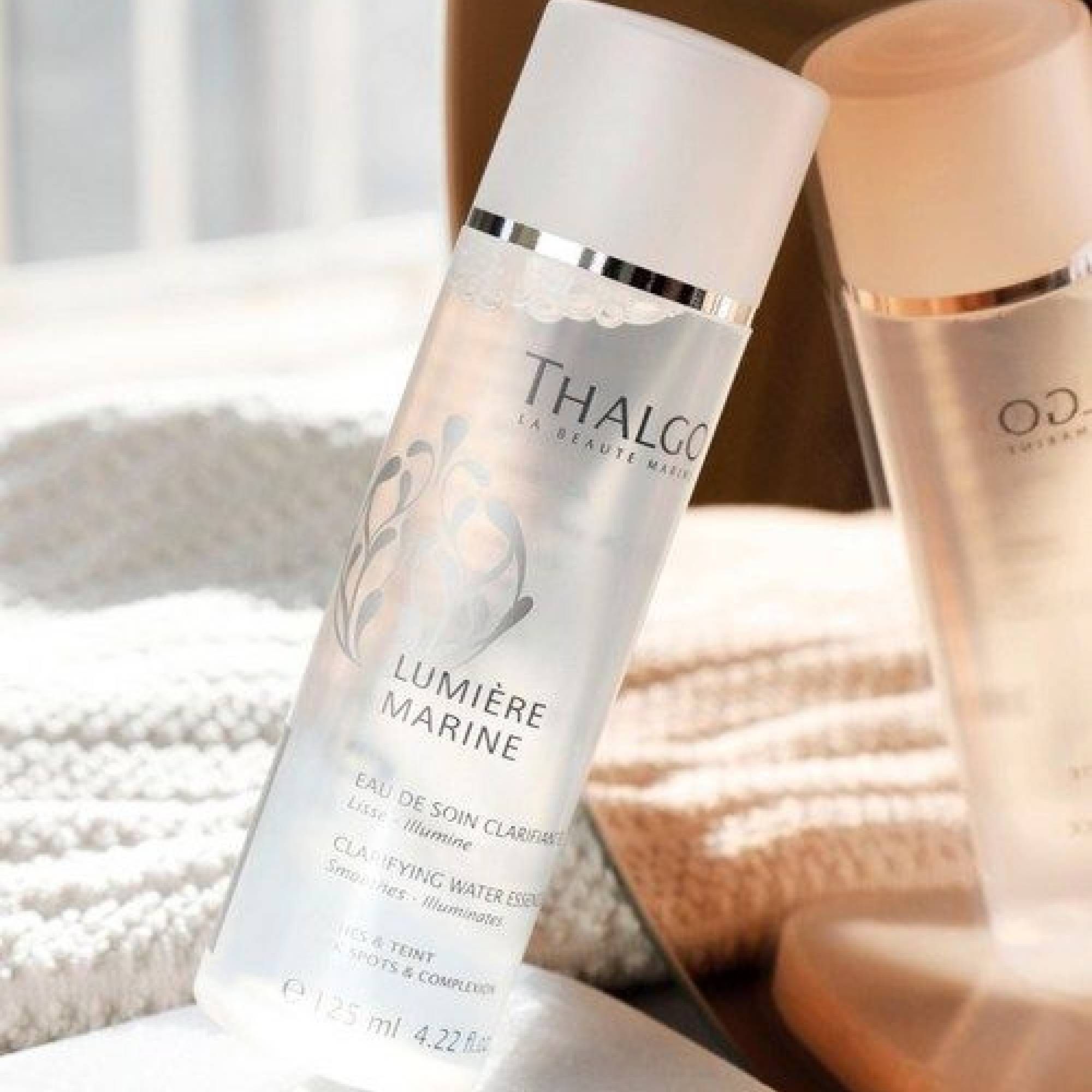 Schräg stehende, transparente Flasche mit silbernem Deckel. Schriftzug: Thalgo, Lumière Marine. Text: Eau de soin clarifiante, Clarifying Water Essence.