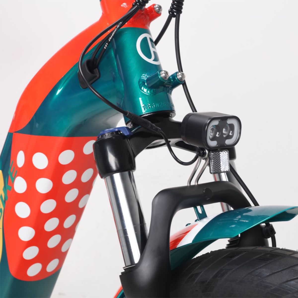 Vordergabel und Scheinwerfer eines E-Bikes. Schwarzer Scheinwerfer, grüne Gabel. Grün-rotes Design. Kabel und Details.