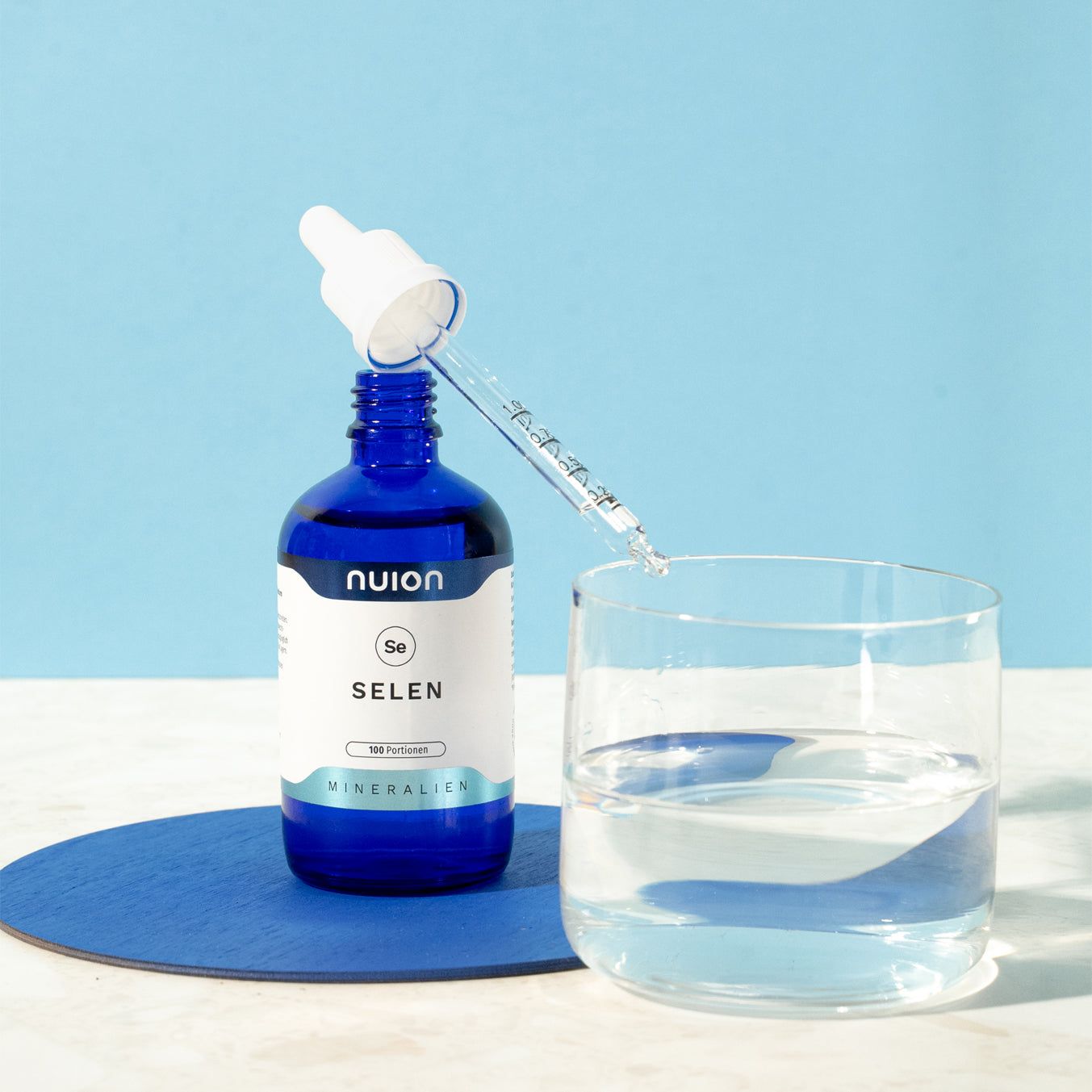 Blaue Tropfflasche mit Selen, daneben ein Glas Wasser.
