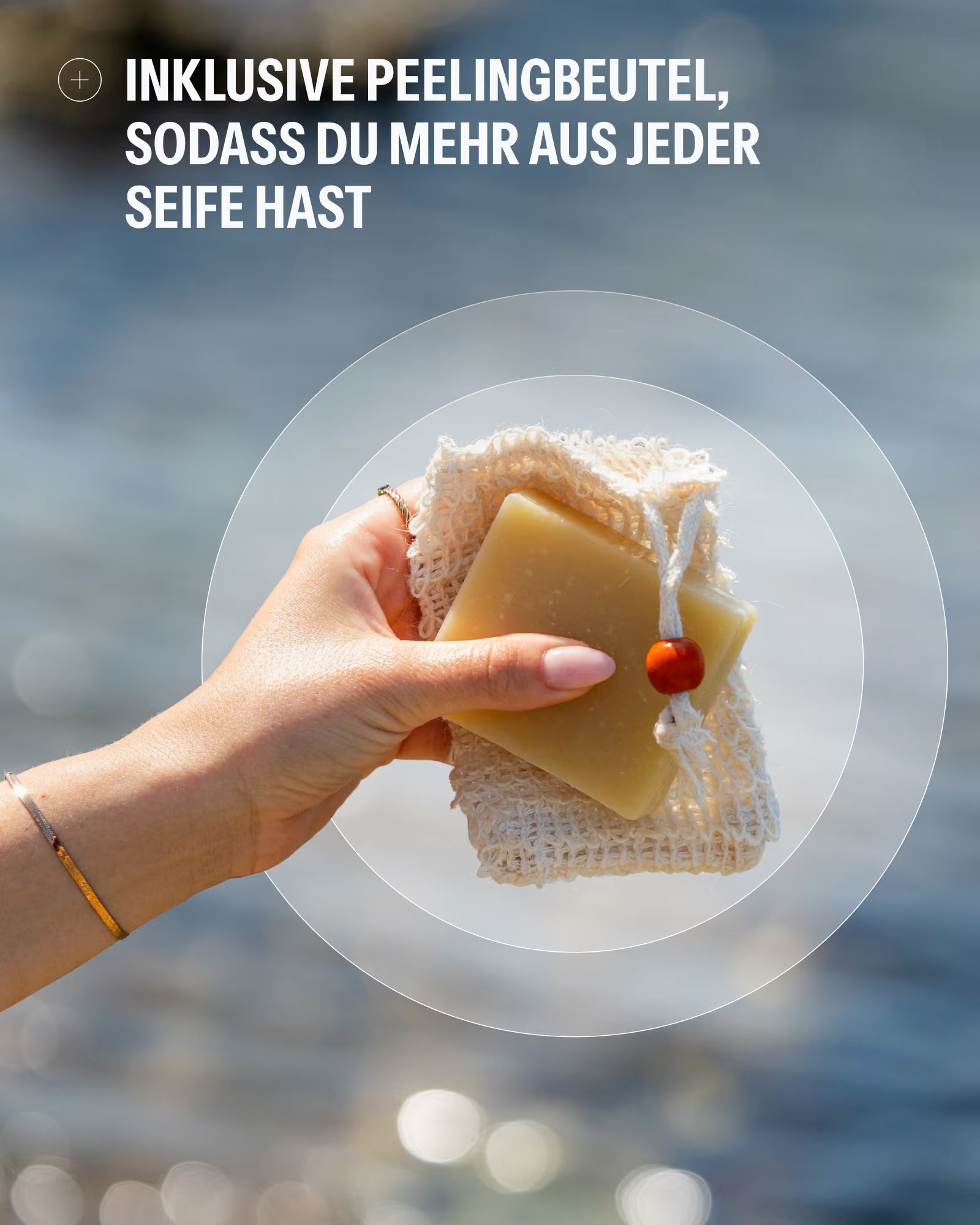 Hand hält Seife in einem Netzbeutel mit Holzperle, nah am Wasser.