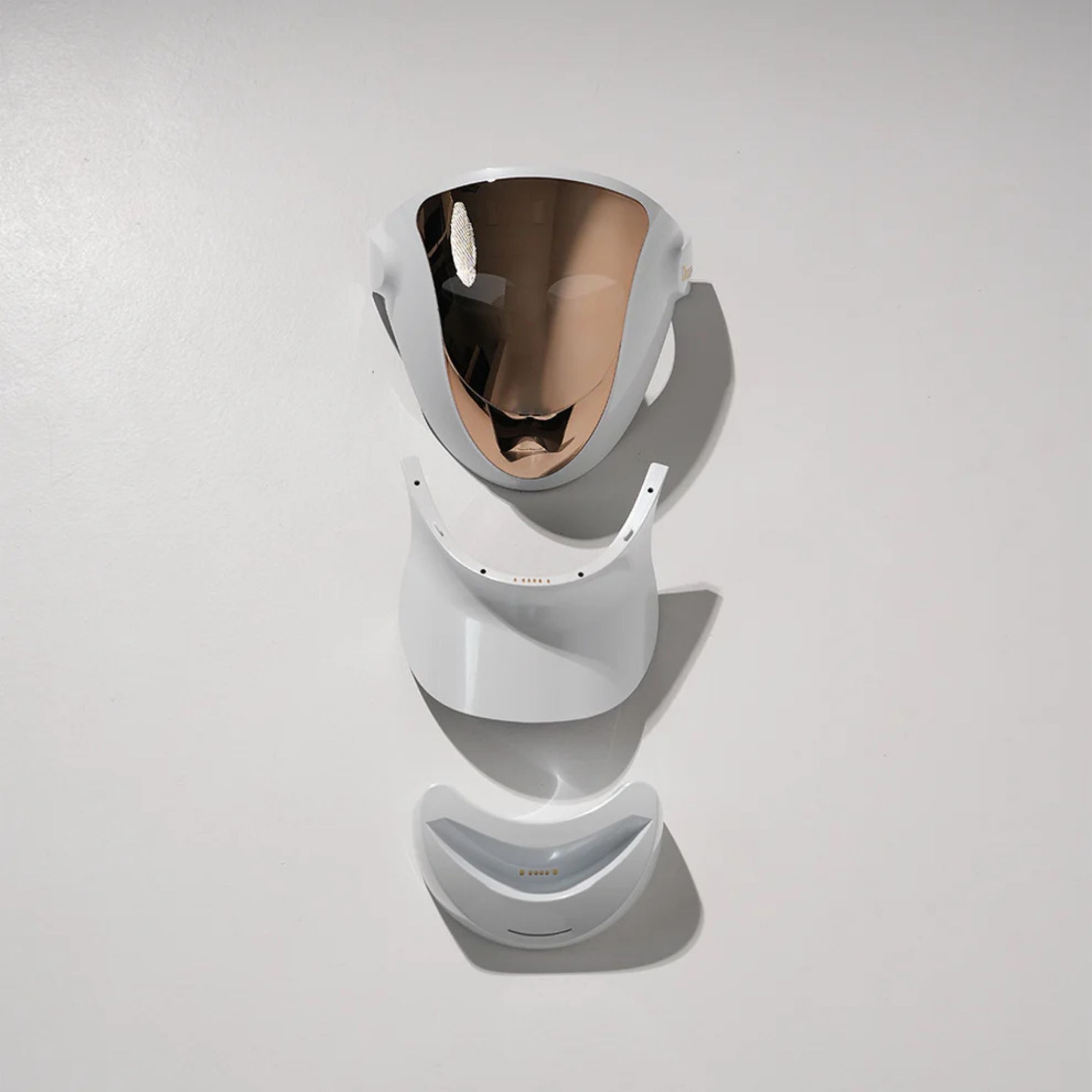 Zerlegte Gesichtsmaske. Weißes Gehäuse mit goldfarbener Oberfläche. Besteht aus drei Teilen: Maske, Halsansatz, Kinnteil.