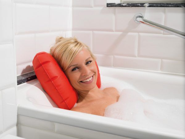 Rotes, aufblasbares Badewannenkissen. Frau in Badewanne mit Schaum. Kissen stützt den Kopf.