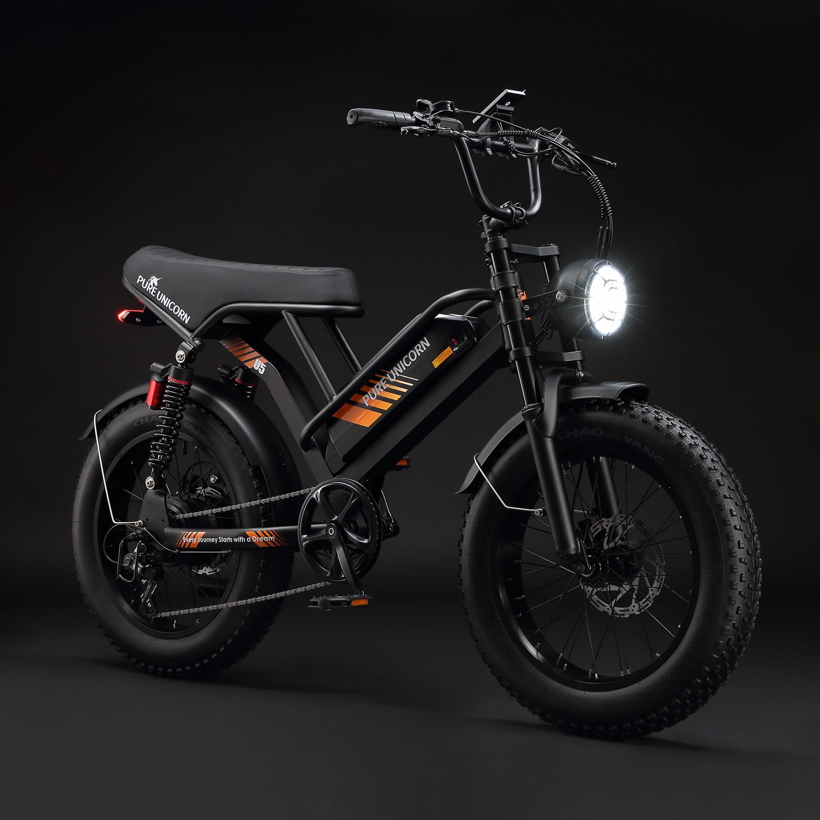 Schwarzes Elektrofahrrad mit breiten Reifen, orangefarbenen Akzenten und dem Schriftzug PURE UNICORN. Scheinwerfer leuchtet.