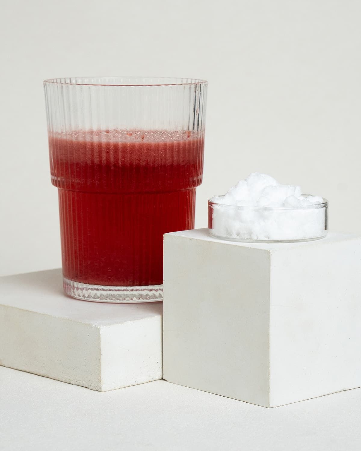 Ein Glas roter Saft und ein kleiner Behälter mit weißem Pulver auf weißen Blöcken.