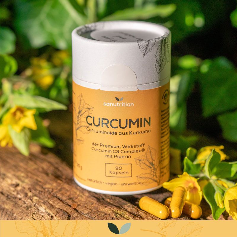 Sanutrition® Curcumin-Dose auf Holz. Daneben Kapseln. Hintergrund: gelbe Blüten und grünes Laub. Aufschrift: Curcumin, 90 Kapseln.