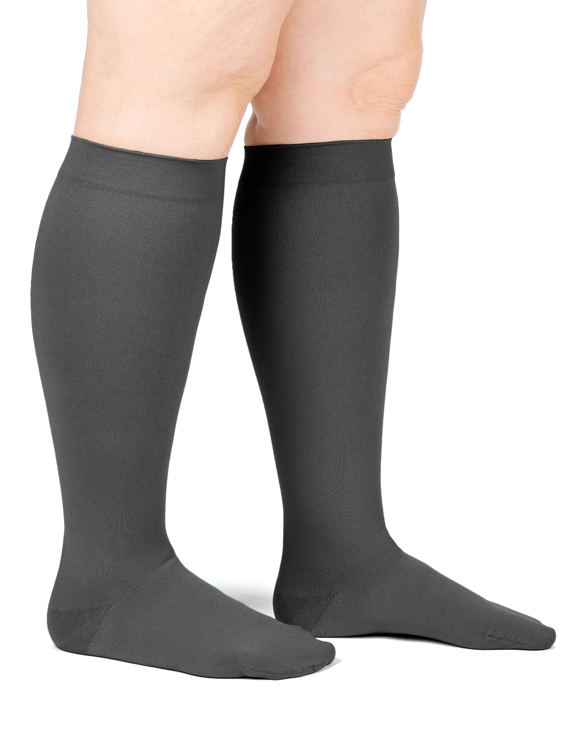 Graue Kompressionsstrümpfe am Bein einer Person. Kniestrümpfe, blickdicht, mit glatter Oberfläche. Blick von der Seite.