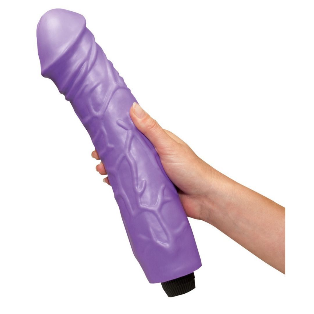 Lila Vibrator, geriffelte Oberfläche, wird von einer Hand gehalten. Schwarzer Sockel. Auf weißem Hintergrund.