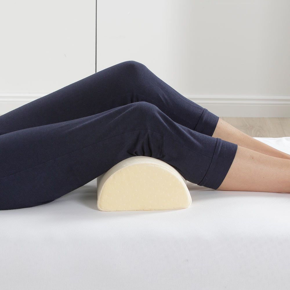 Beine liegen auf weißer Matratze, Lendenkissen darunter. Beige, halbmondförmiges Kissen. Dunkelblaue Hose.