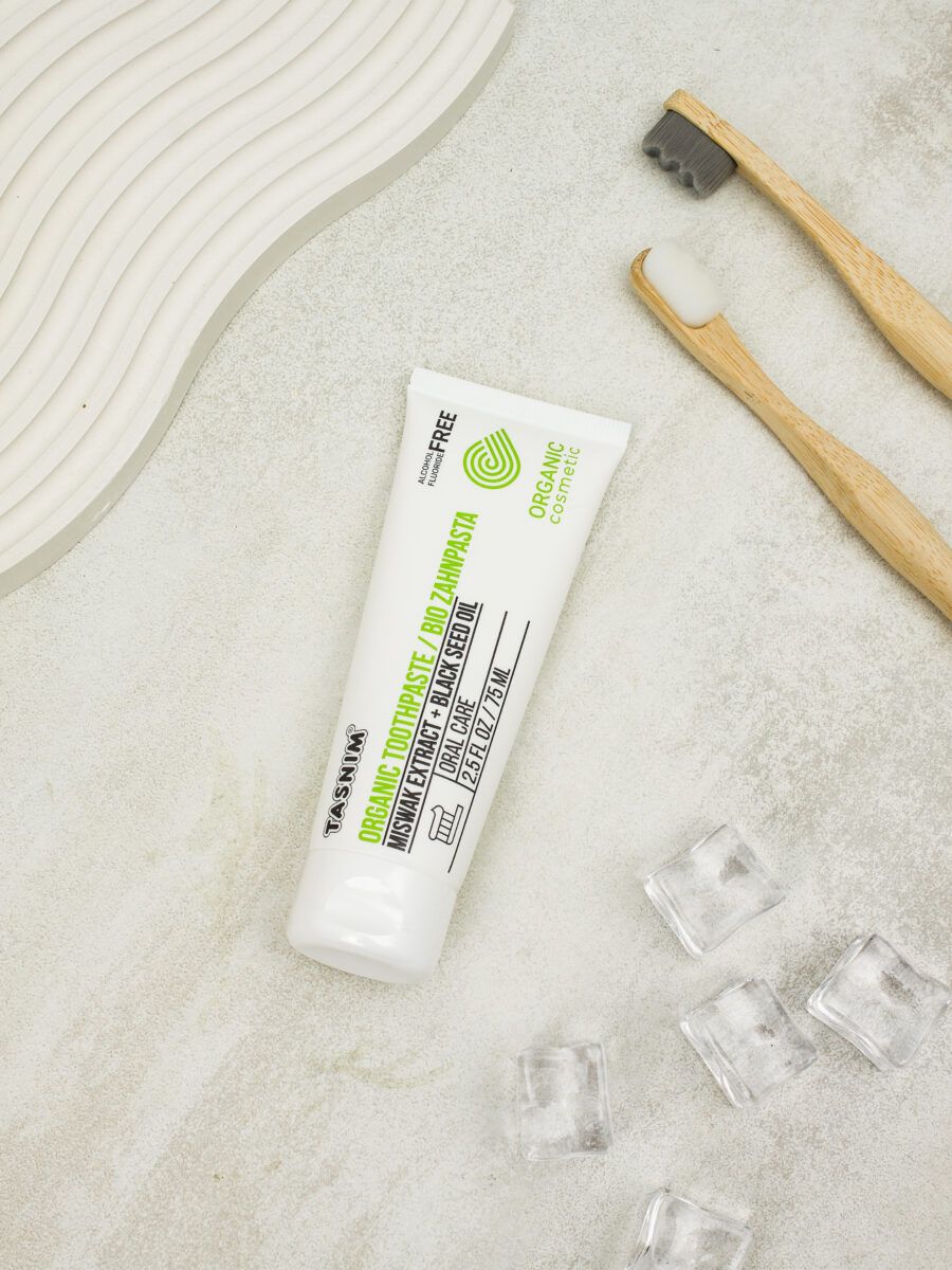 Weiße Zahnpasta-Tube mit grüner Grafik und Schriftzug. Zwei Bambus-Zahnbürsten daneben. Eiswürfel liegen verstreut.