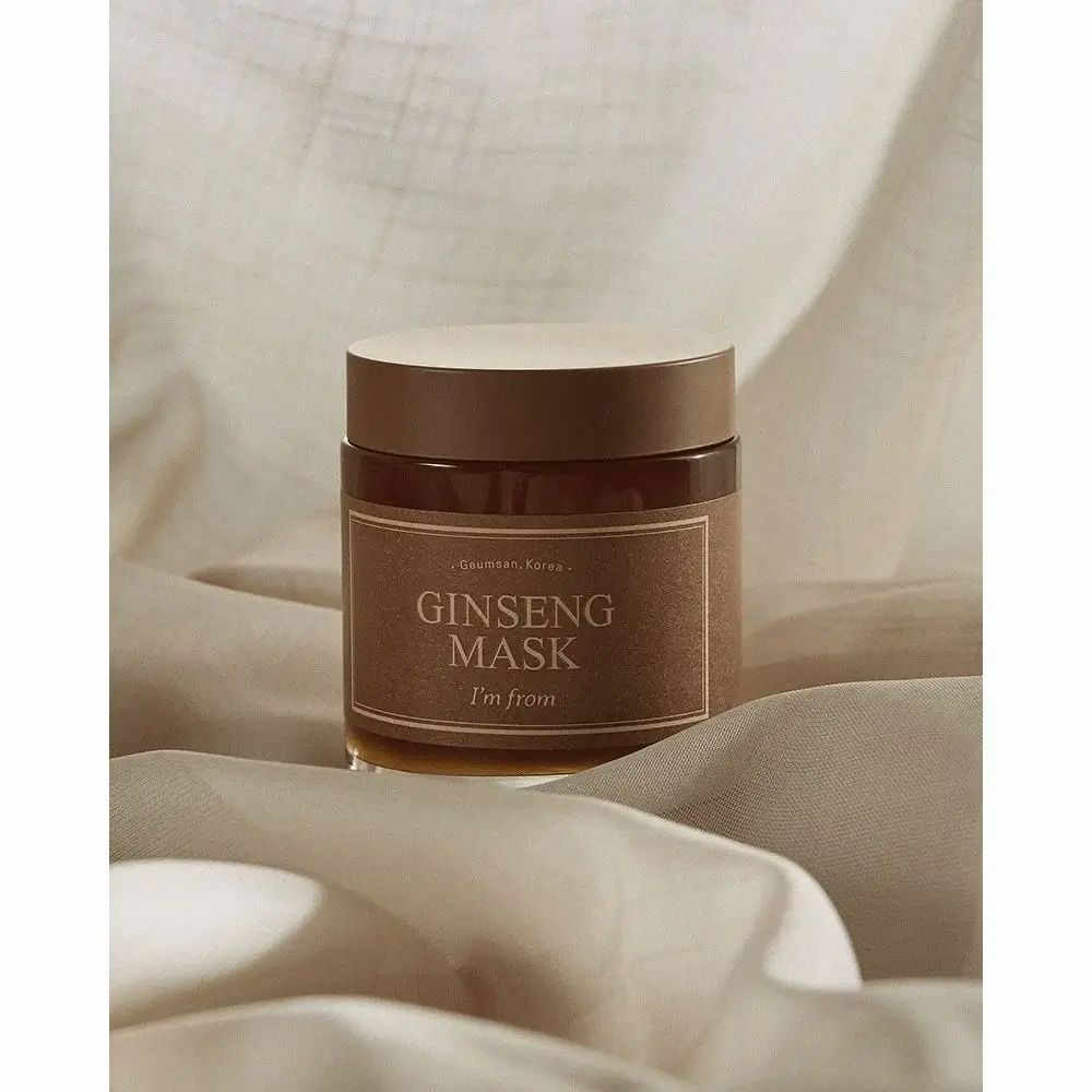 Glasbehälter mit braunem Etikett. Aufschrift: GINSENG MASK, I'm from. Brauner Deckel. Auf weißem Stoff.