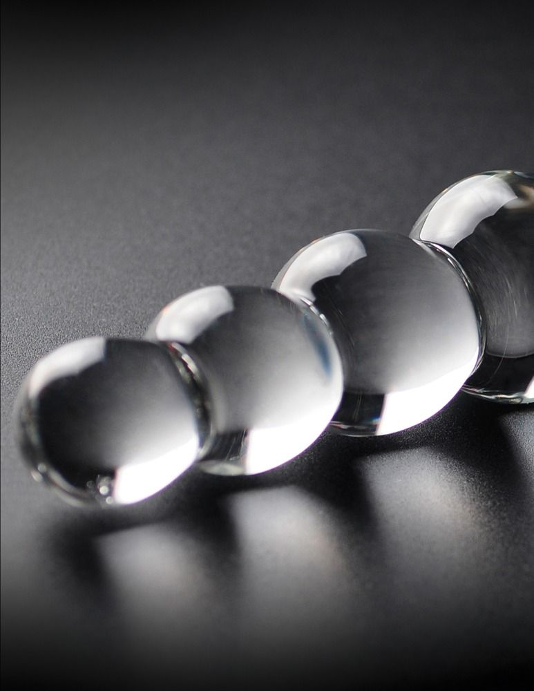 Nahaufnahme von Glasdildo im Kugeldesign. Transparentes Glas, glatte Oberfläche. Schwarzer Hintergrund.