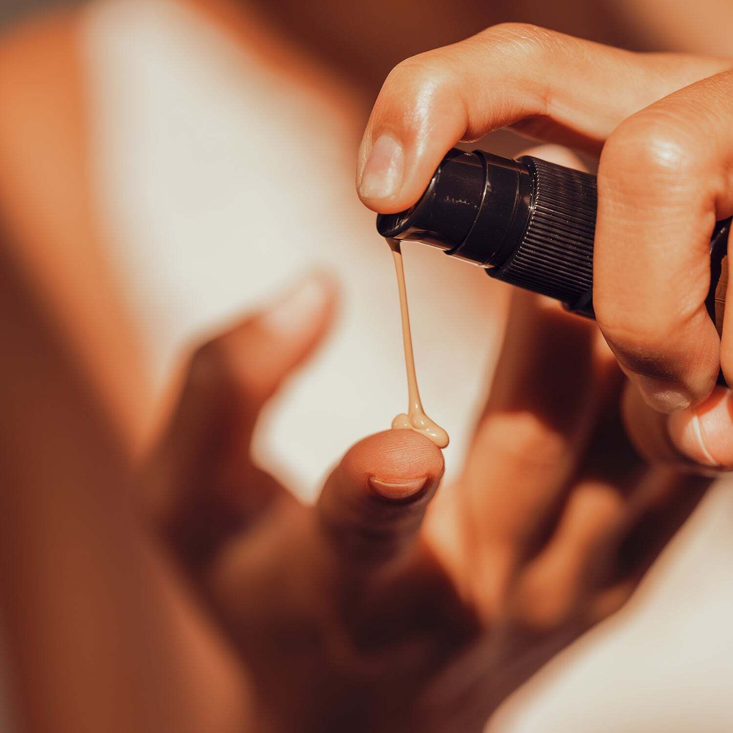 Nahaufnahme einer Hand, die Serum auf einen Finger aufträgt. Schwarzer Pumpkopf, Serum in hellem Farbton.