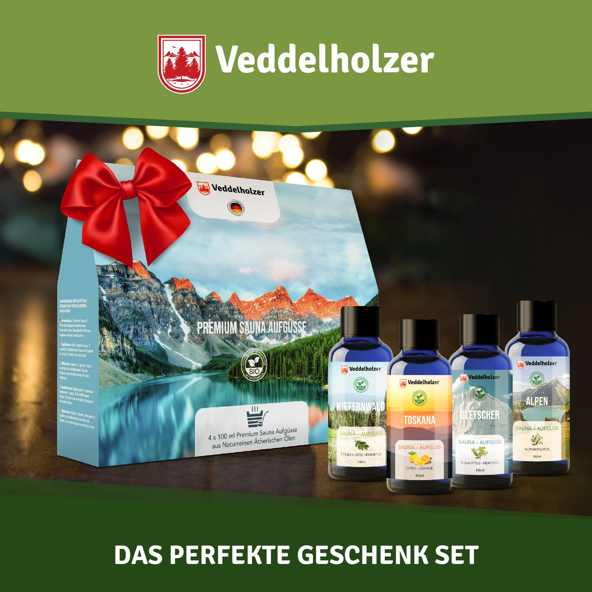 Geschenkset mit Saunaaufgüssen, roter Schleife. Vier blaue Flaschen, Verpackung mit Berglandschaft. Veddelholzer Logo.