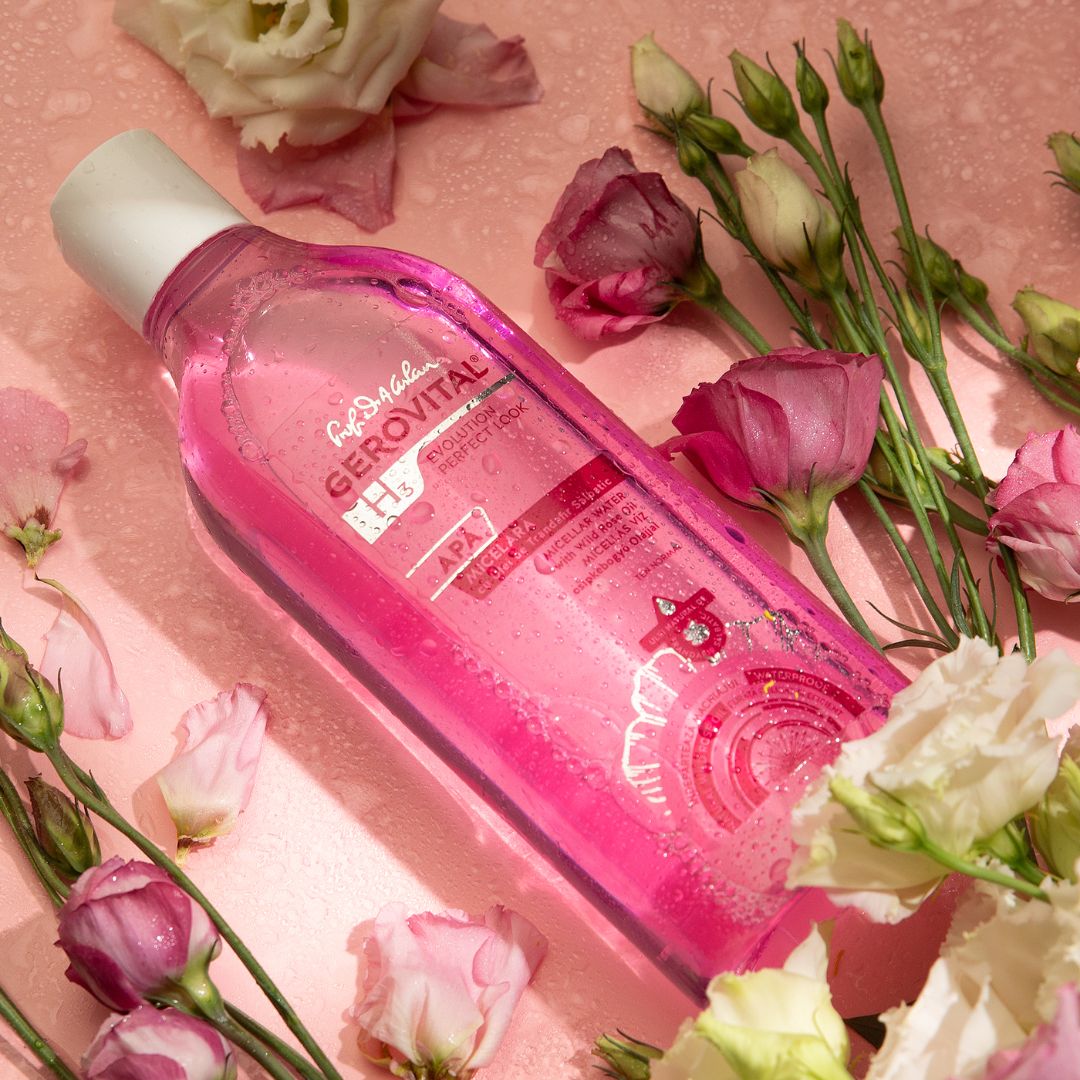Rosa Flüssigkeit in einer transparenten Flasche mit weißem Deckel. Aufkleber mit Text: Gerovital, Micellare Wasser. Umgeben von Blumen.