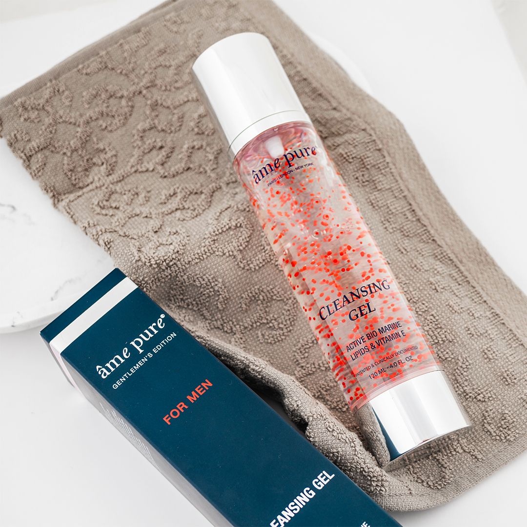Transparante fles met rode deeltjes en blauwe doos. Opschrift: âme pure Cleansing GEL. Op een handdoek.