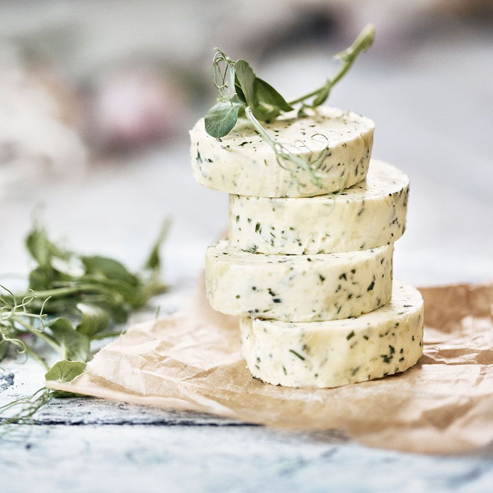 Gestapelte Kräuterbutter-Rollen. Auf braunem Papier. Mit Zitronenthymian. Sichtbare Kräuter.