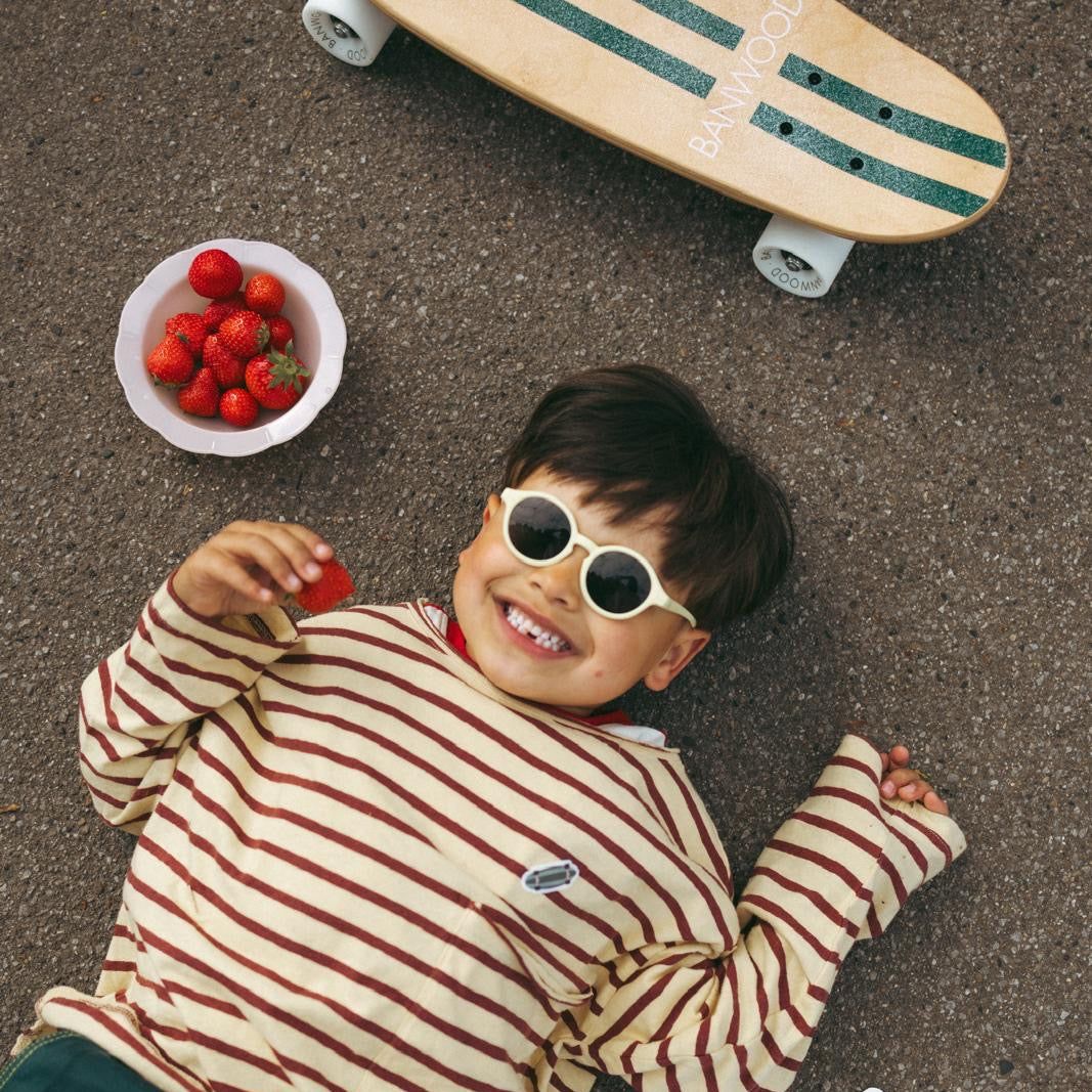 Junge mit Sonnenbrille liegt auf dem Boden neben Skateboard und Erdbeeren.