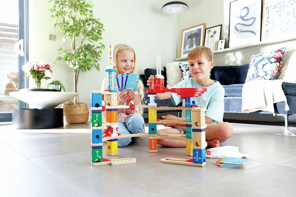 Zwei Kinder spielen mit einem Quadrilla-Set. Das Set besteht aus Holzblöcken, Bahnen und Kugeln. Kinder halten Karten.