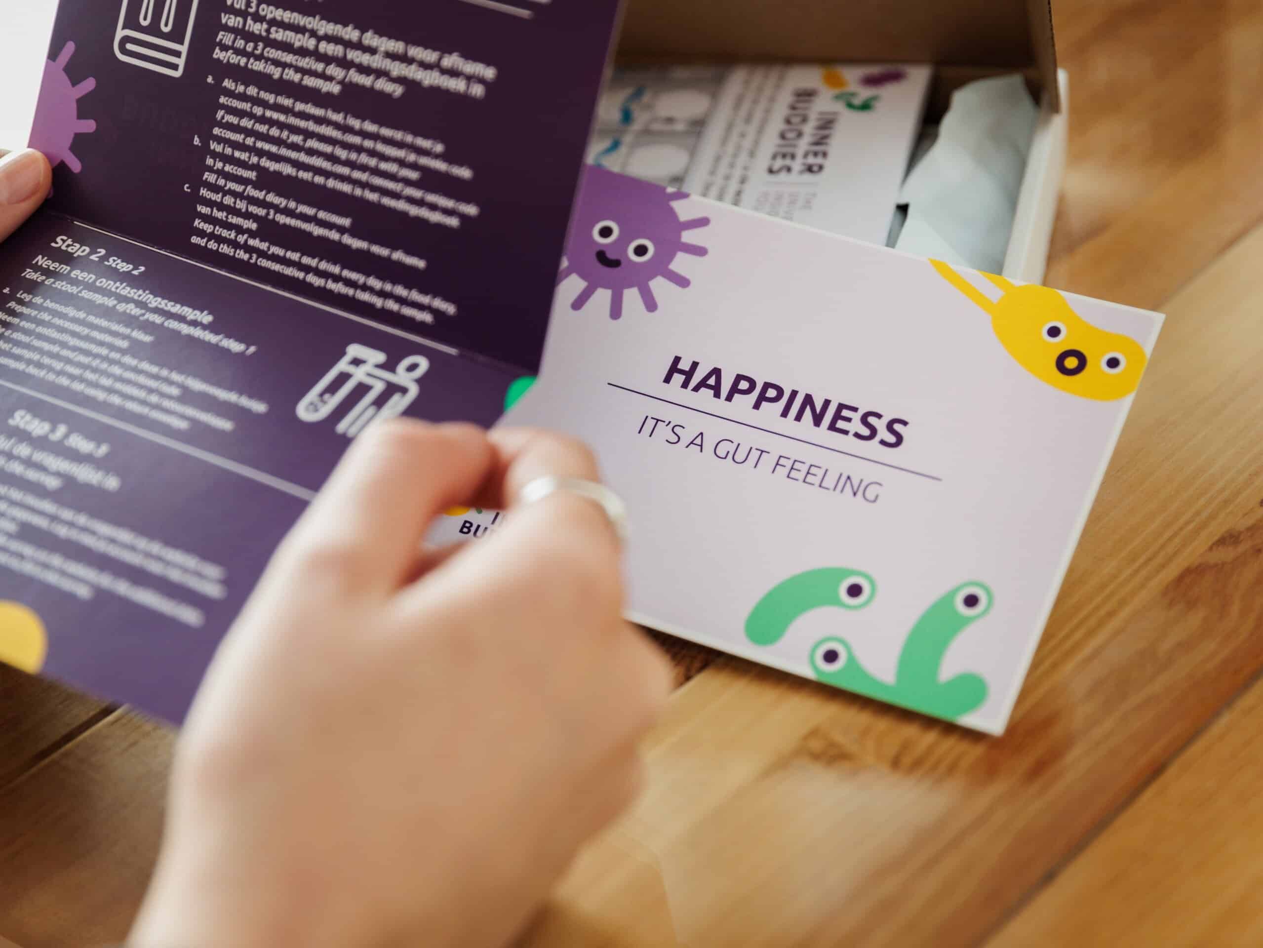 Person öffnet eine Broschüre mit Anleitungen und einer Karte mit der Aufschrift 'Happiness - It's a Gut Feeling'.