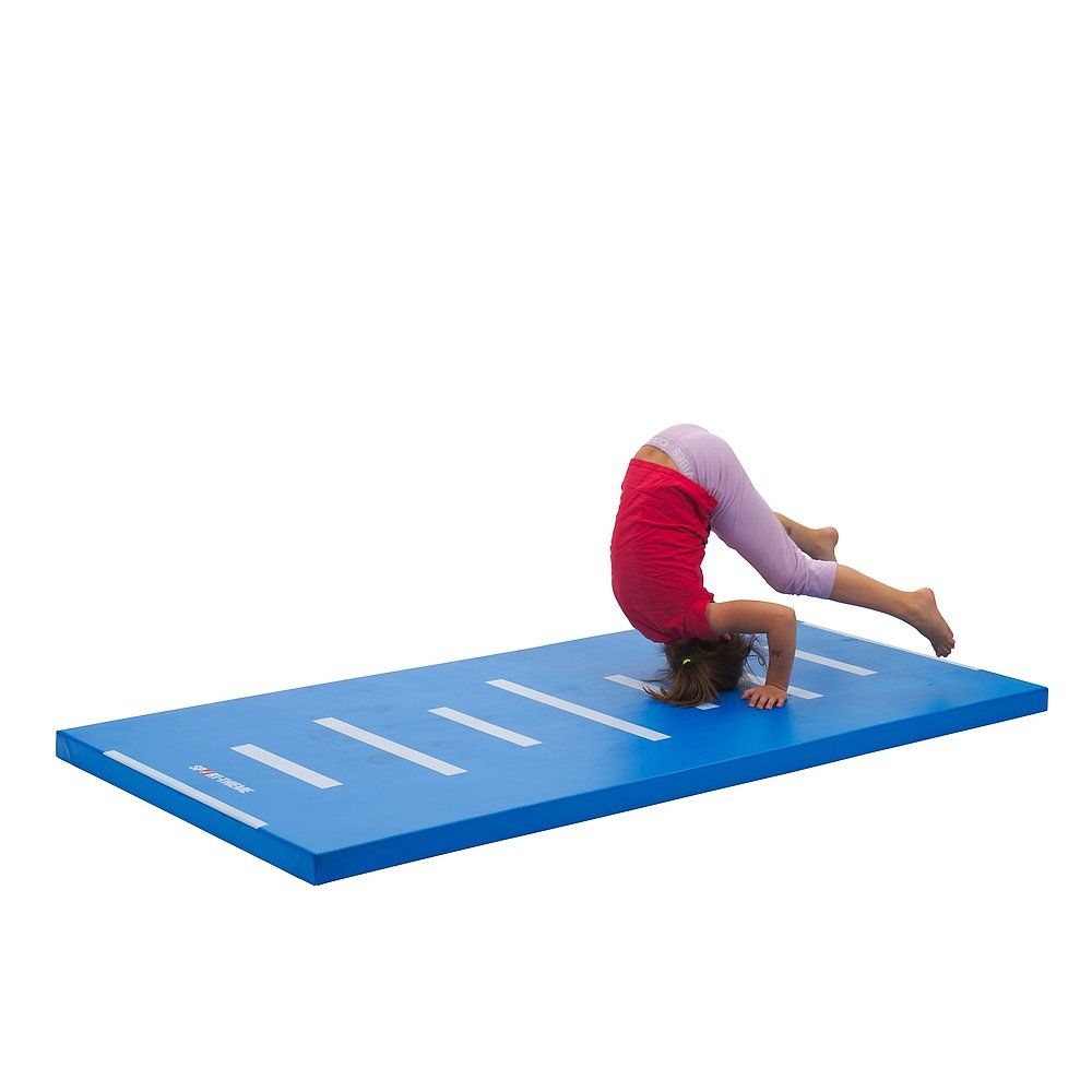 Kind macht Handstand auf blauer Turnmatte mit weißen Streifen. Matte liegt auf weißem Hintergrund.