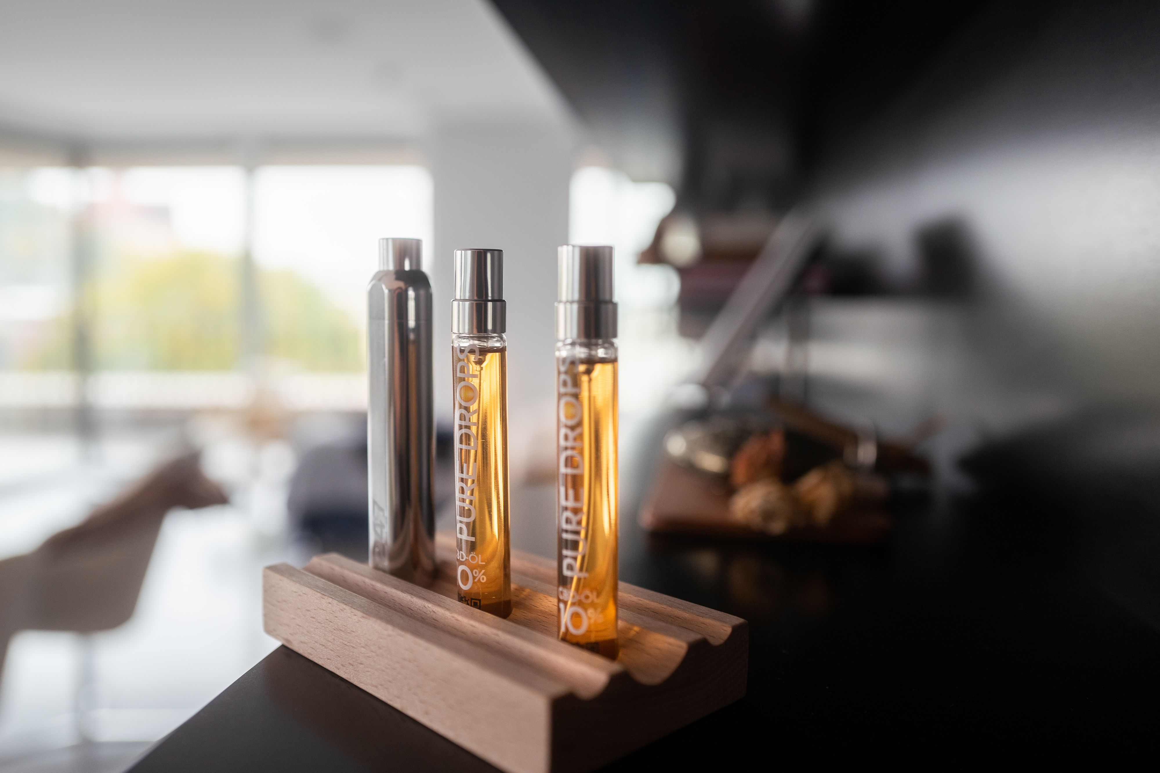 Due flaconi con liquido dorato, un flacone argento, su supporto in legno. Scritta: "PURE DROPS 10% CBD-ÖL".