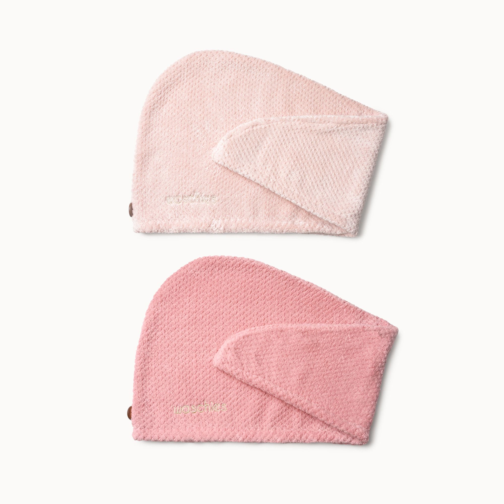 Zwei rosa Haarturbane aus Mikrofaser. Oben hellrosa, unten pink. Beide haben eine rechteckige Lasche und ein kleines Logo.