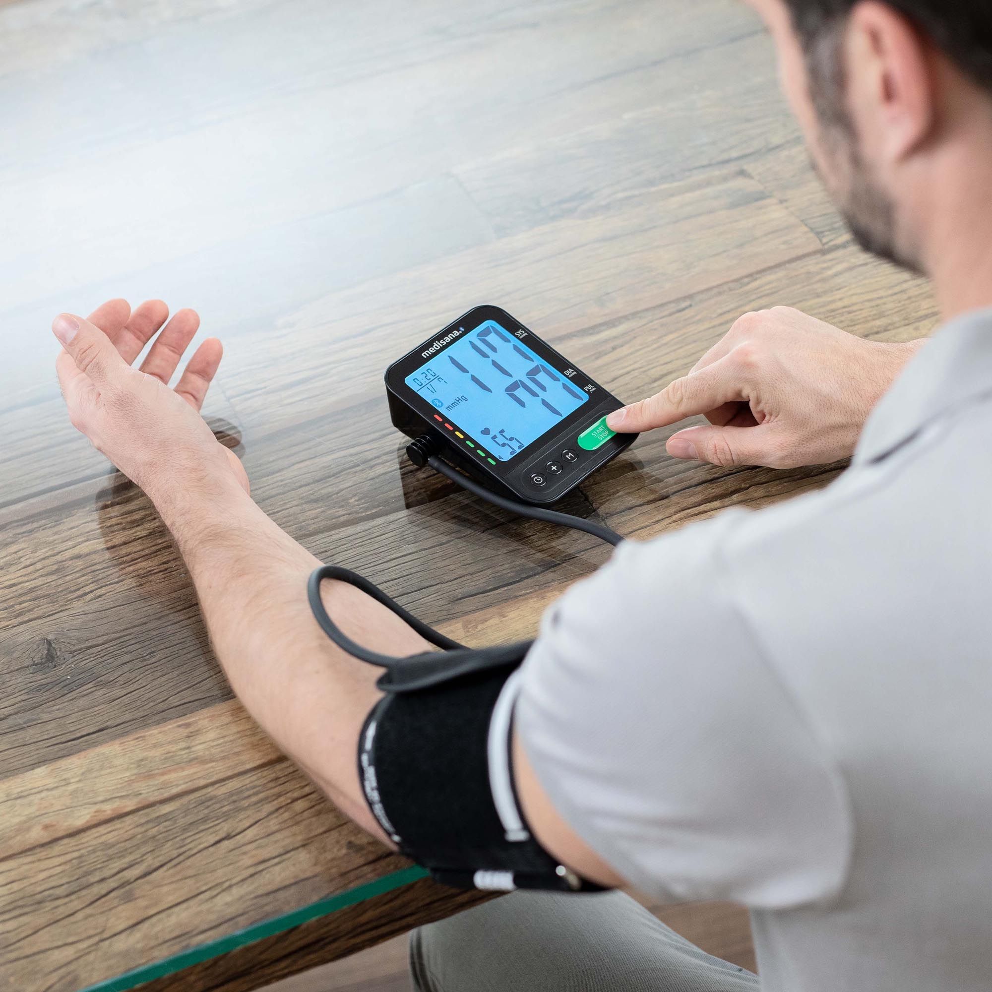 Bloeddrukmeter om de arm van een man. Apparaat toont meetwaarden. Manchet om de arm. Man drukt op de startknop.