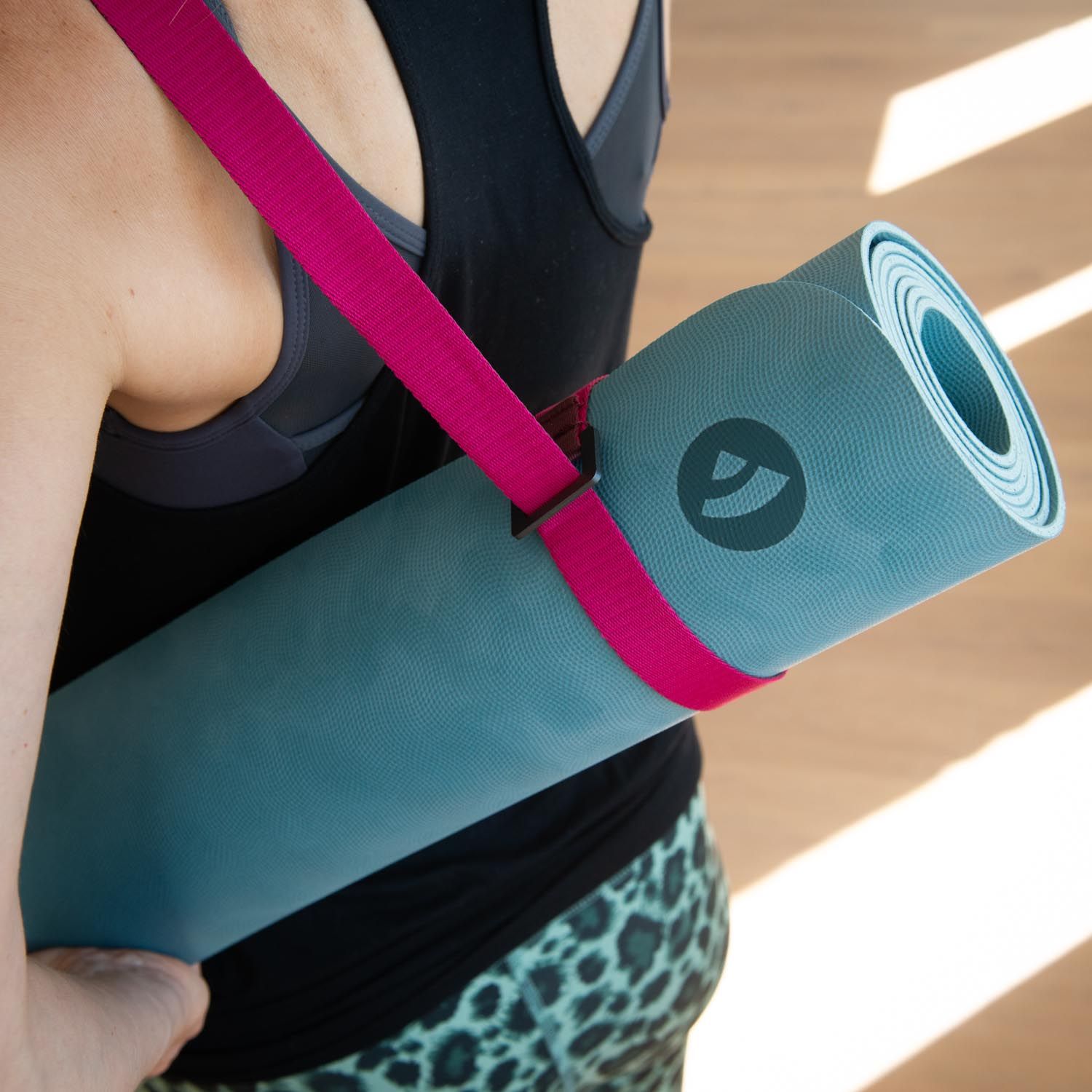 Person trägt gerollte Yogamatte mit pinkfarbenem Tragegurt. Logo auf der Matte. Person von hinten.