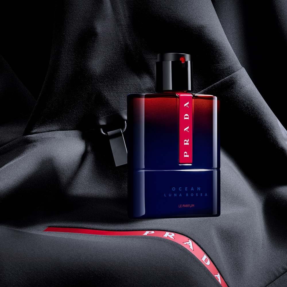 Flakon Prada Luna Rossa Ocean Le Parfum auf schwarzem Stoff. Rotes Prada-Logo. Schwarzer Hintergrund.