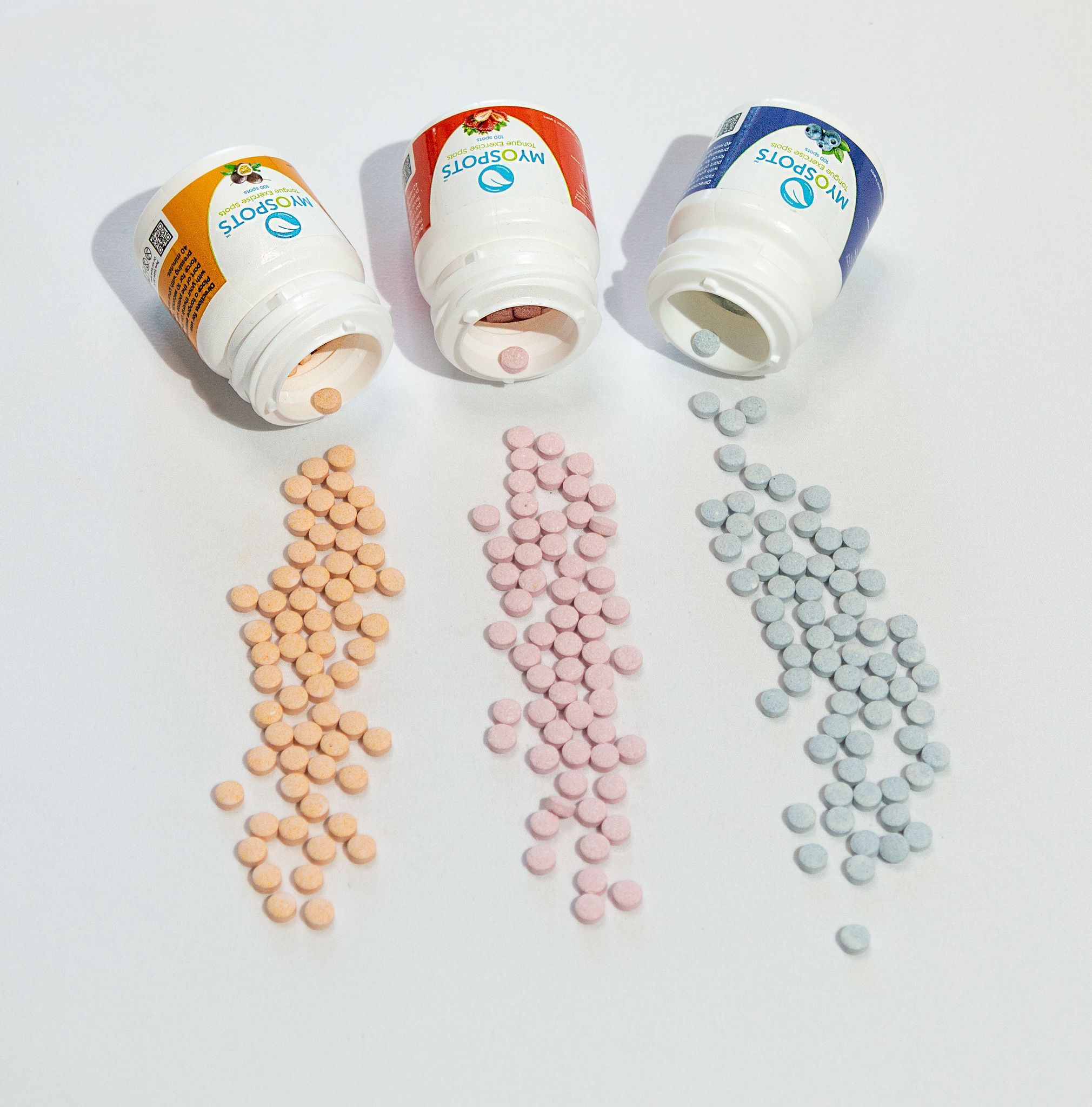 Drei geöffnete Flaschen mit Tabletten. Tabletten in Orange, Rosa und Blau. Produktname auf den Flaschen.