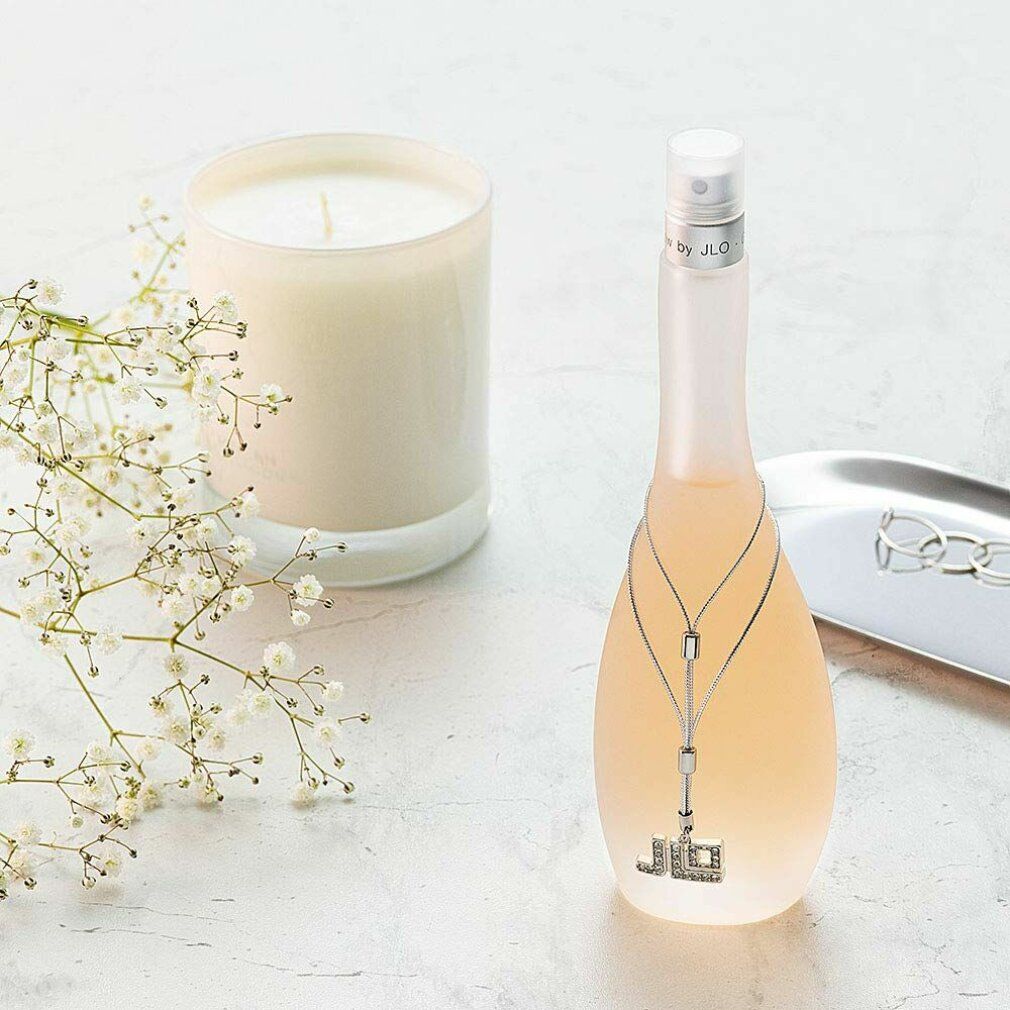 Eau de Toilette-Flakon neben Kerze und Dekoration. Flakon mit silberfarbener Kette und JLo-Logo. Kerze in Glas.