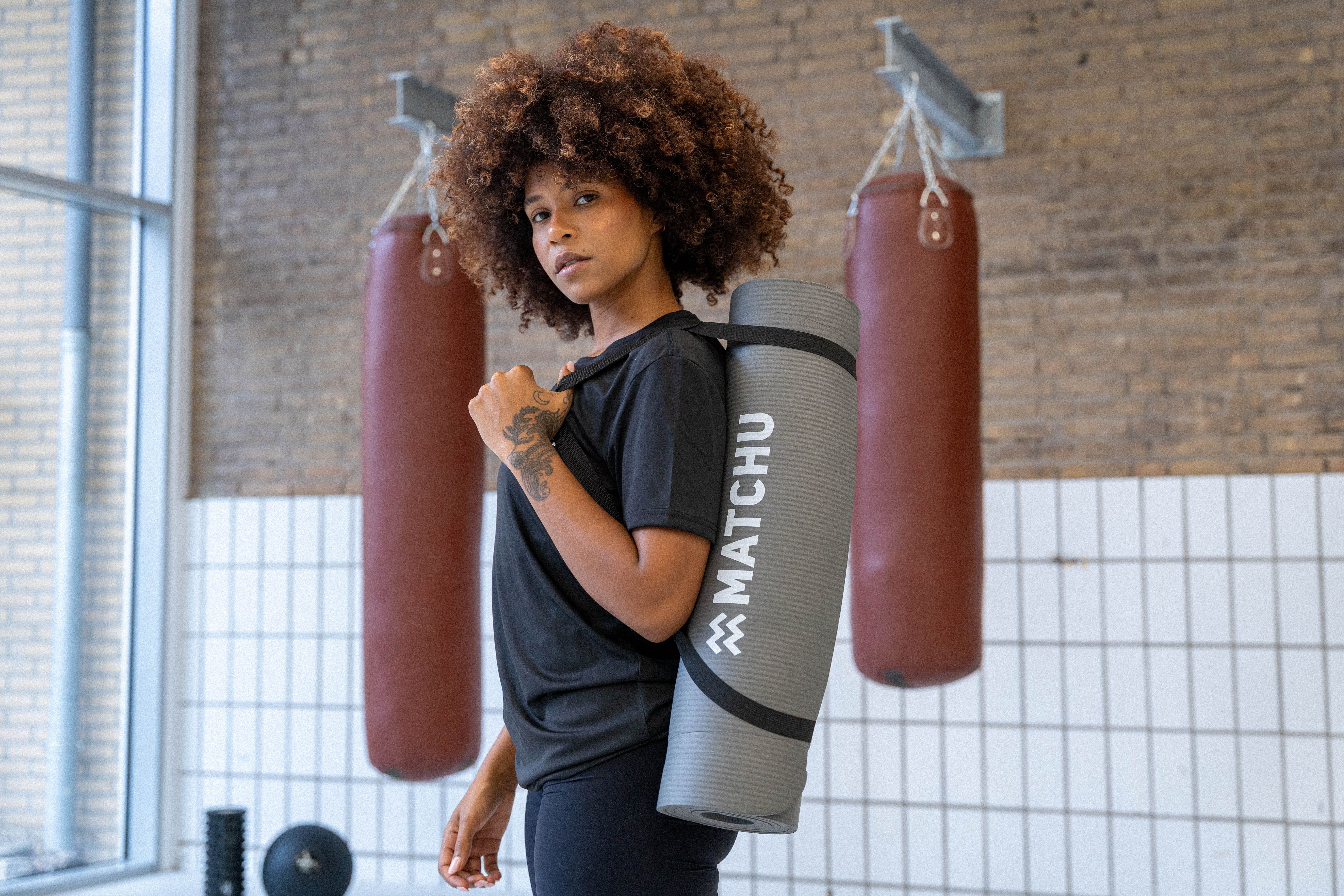 Frau mit Fitnessmatte über der Schulter. Auf der Matte steht "MATCHU".