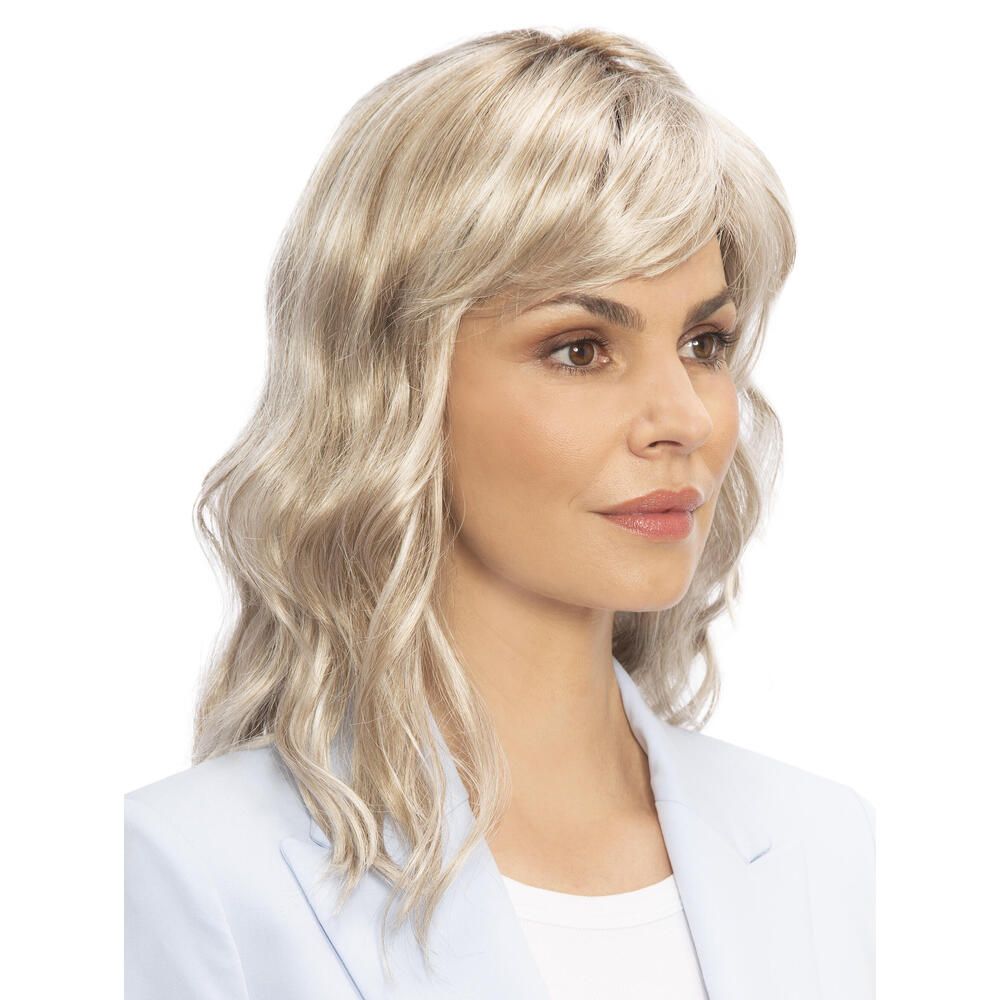 Perücke Kiky von trendhair. Blond, gewellt, mit Pony. Frau trägt hellblaues Jackett. Dreiviertelansicht.