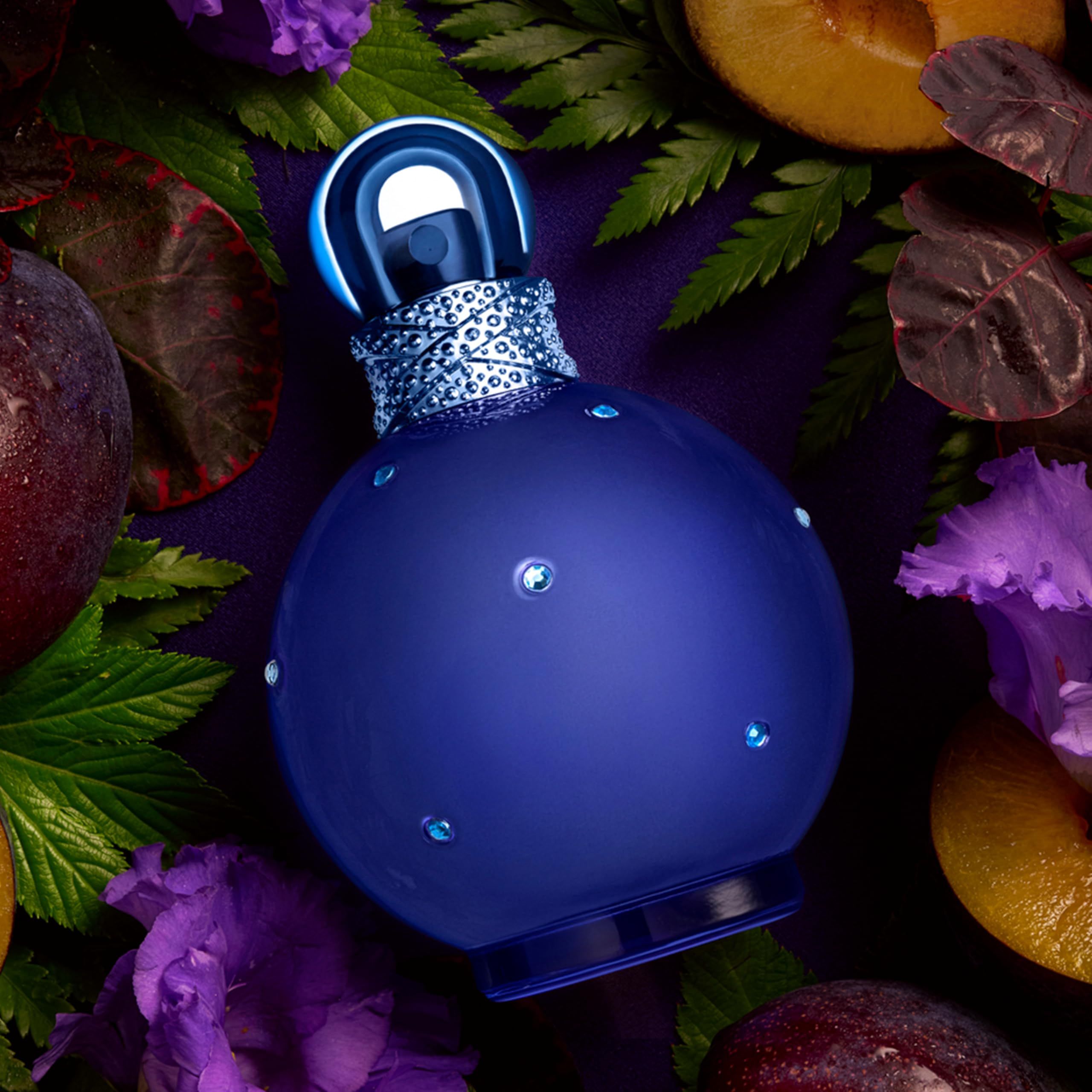 Dunkelblaue Flasche mit Sprühkopf, umgeben von Pflaumen und Blättern. Dekorative Anordnung.