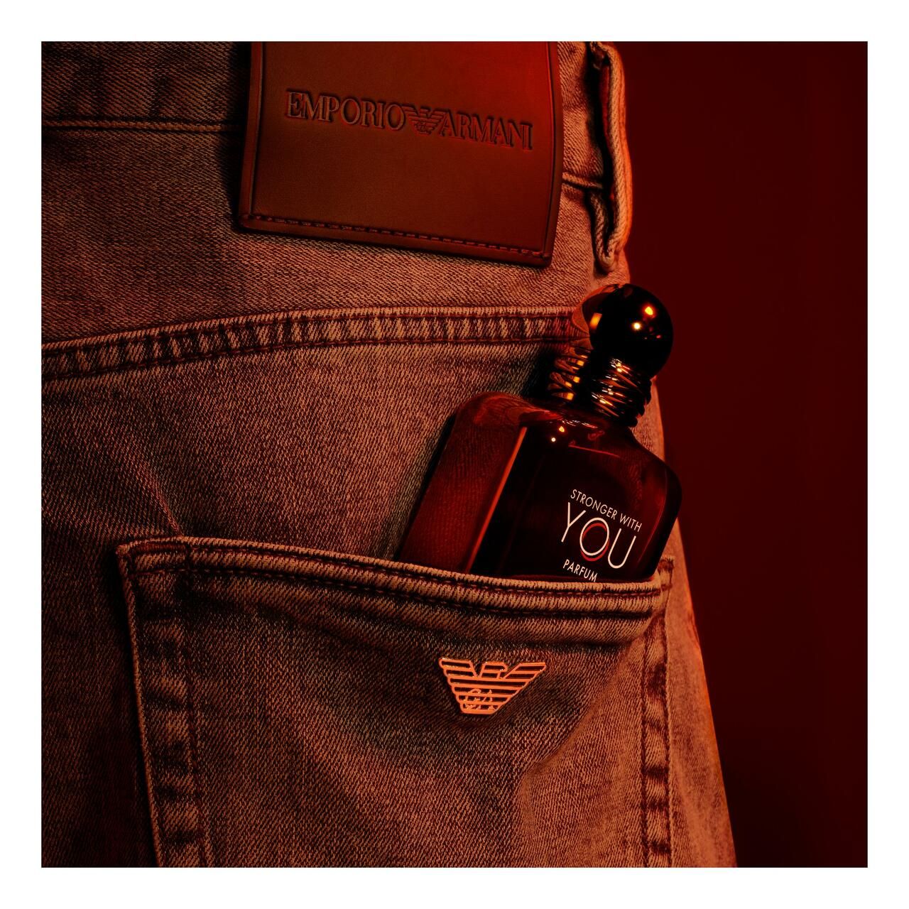 Rotbrauner Parfümflakon in Jeans-Hosentasche. Jeans mit Lederetikett und Markenlogo.