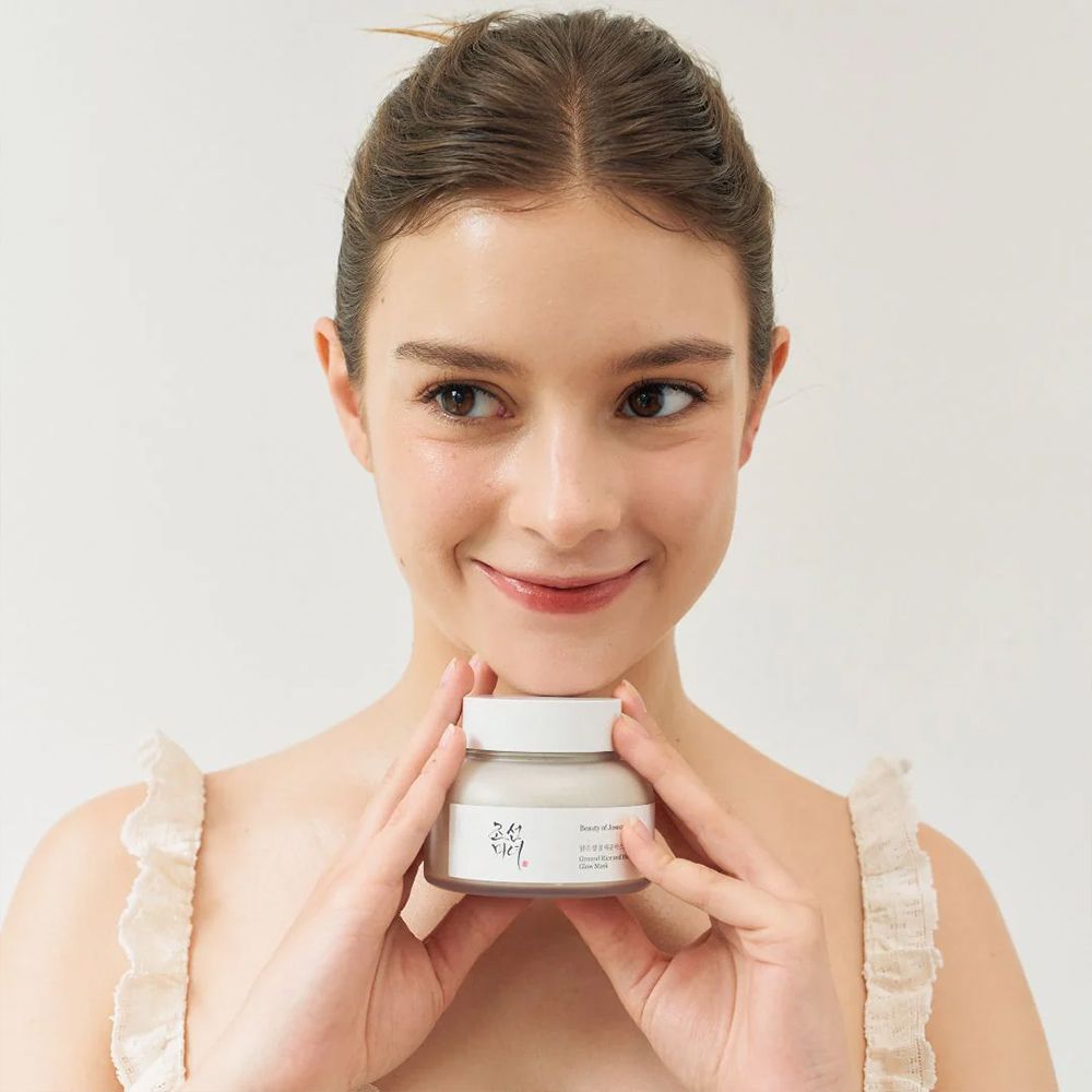 Junge Frau hält einen Behälter der BEAUTY OF JOSEON Ground Rice and Honey Glow Mask.