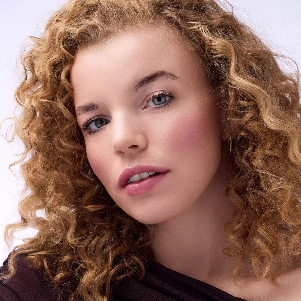 Porträt einer Frau mit Locken. Rouge auf den Wangen. Helle Haut, blaue Augen.