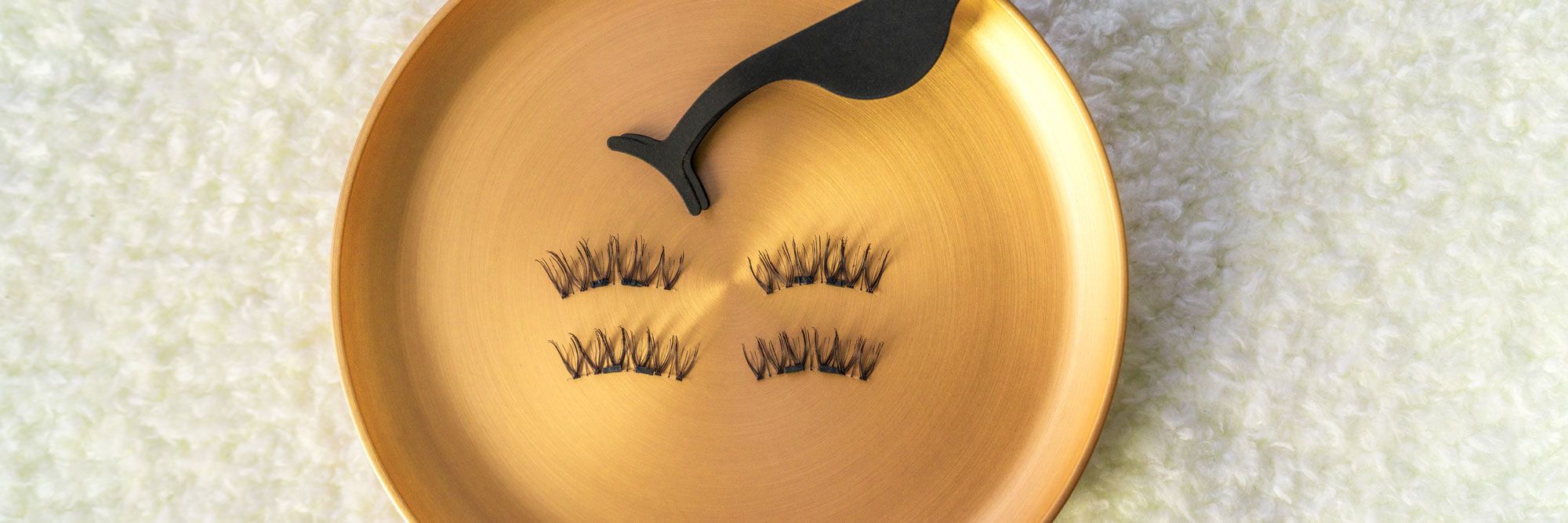 Wimpern-Applikator und Wimpern auf goldener Oberfläche. Logo: K.