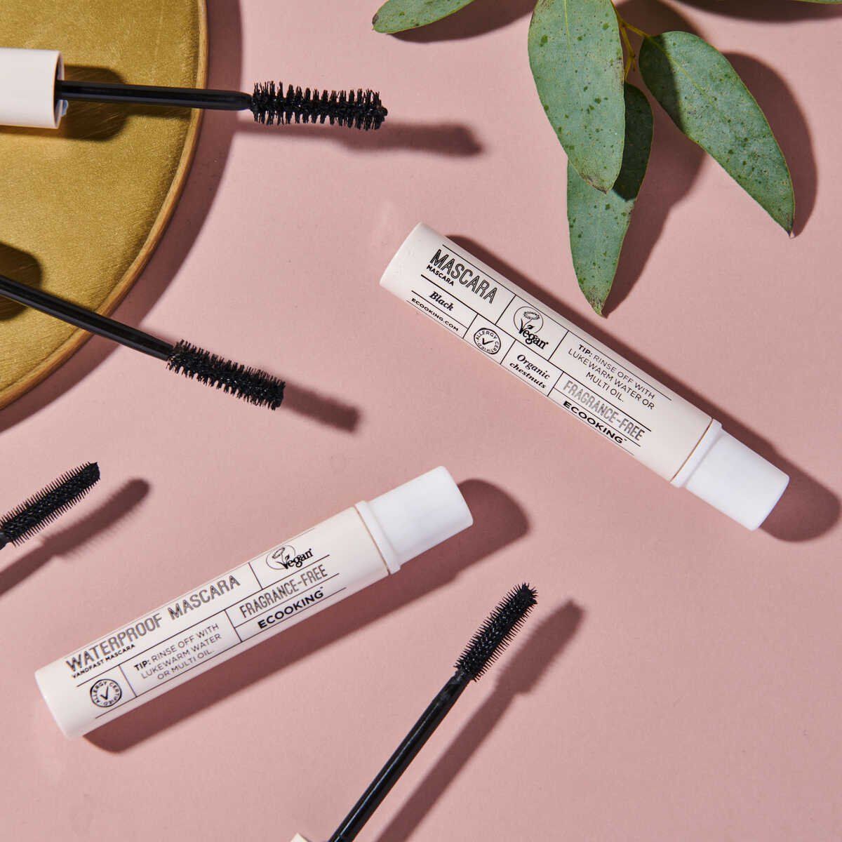 Mehrere Mascara-Tuben und Bürsten auf rosa Oberfläche. Weiße Deckel, schwarze Bürsten. Vegan-Logo und Text: „WATERPROOF MASCARA“ und „FRAGRANCE-FREE“.
