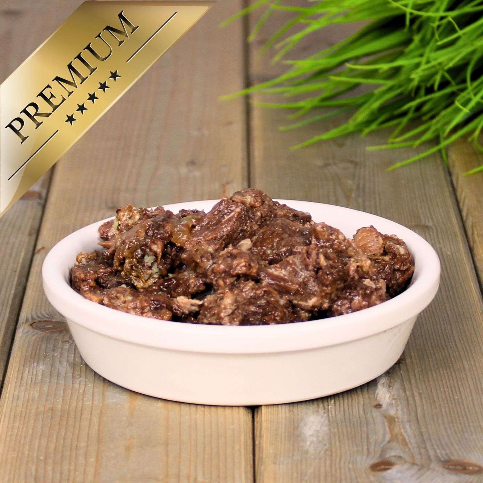 Eine weiße Schale gefüllt mit rohem Fleisch auf einem Holztisch. Ein goldener Banner mit der Aufschrift "PREMIUM" ist oben links angebracht.
