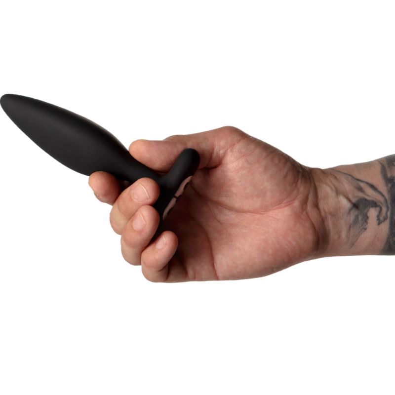 Hand hält schwarzen Analplug. T-Form, abgerundete Spitze. Tattoo auf dem Arm.