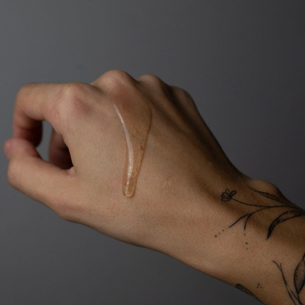 Hand mit Tattoo. Gelartige Flüssigkeit auf der Haut. Grauer Hintergrund.