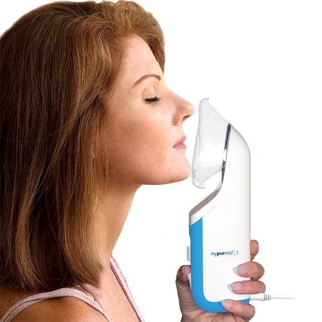 Frau benutzt Inhalator. Inhalator weiß-blau, mit Mundstück. Frau mit geschlossenen Augen, Inhalator am Gesicht. Kabel sichtbar.