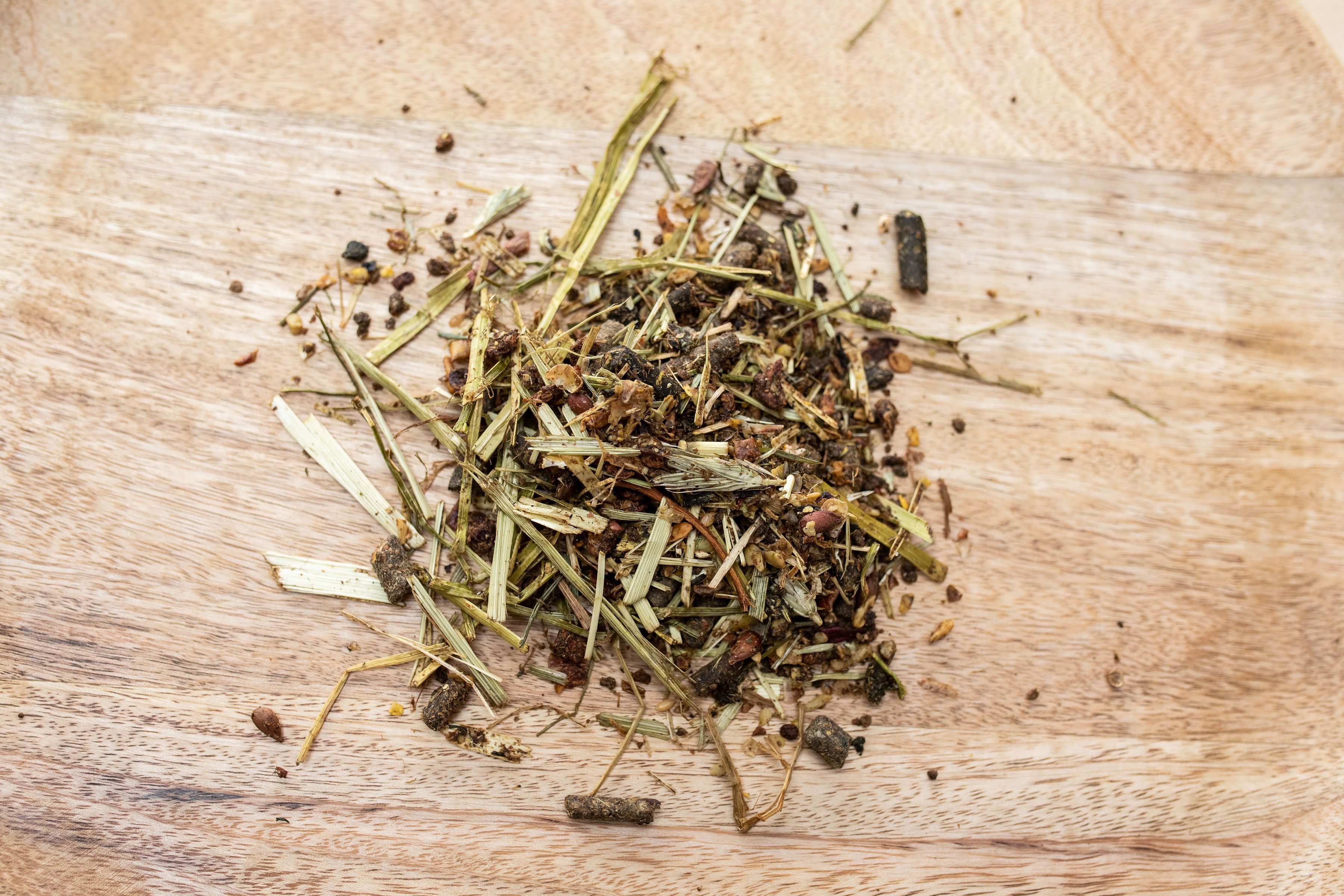 Haufen von Müsli auf Holzbrett. Enthält Kräuter, Samen und Pellets. Nahaufnahme.