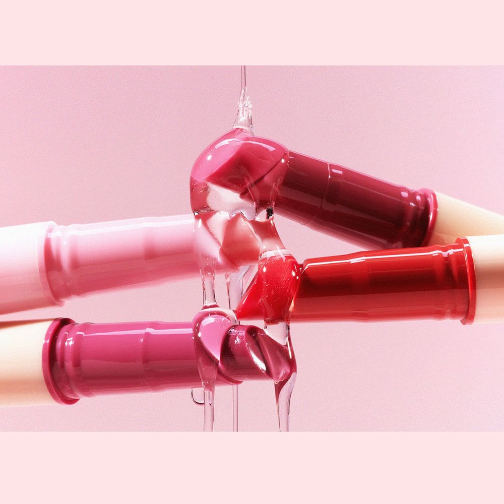 Mehrere Lippenstifte in verschiedenen Rosatönen mit tropfender Flüssigkeit.