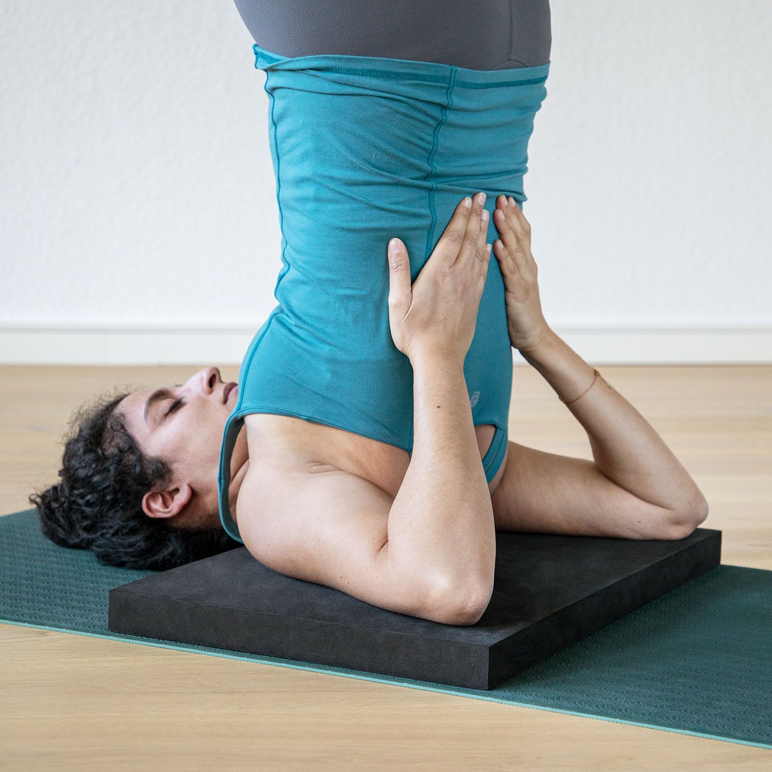 Person in Yoga-Position auf schwarzem Yoga-Block XL. Auf Yogamatte. Block unter Schultern.