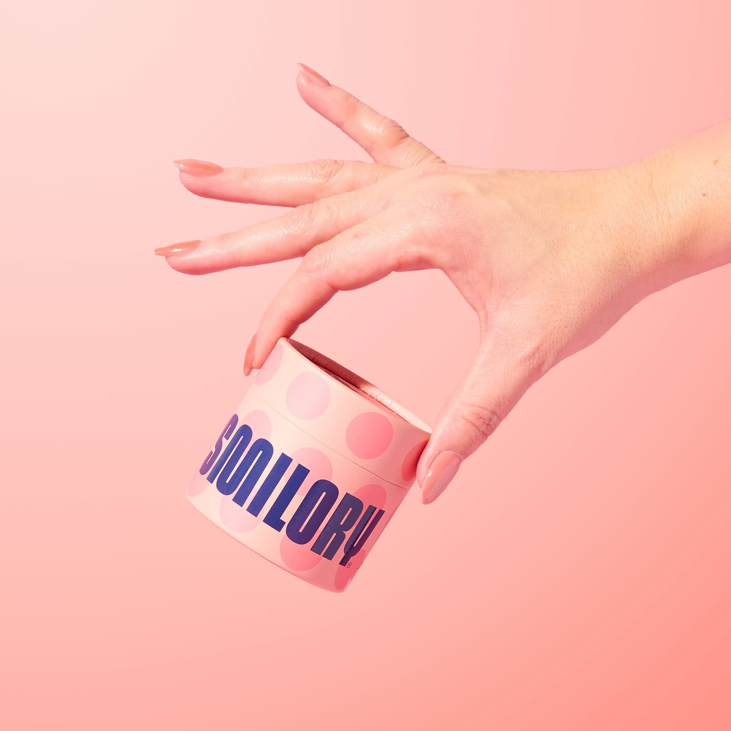Hand hält einen runden Behälter mit dem Schriftzug "SMILORY". Rosa Hintergrund.