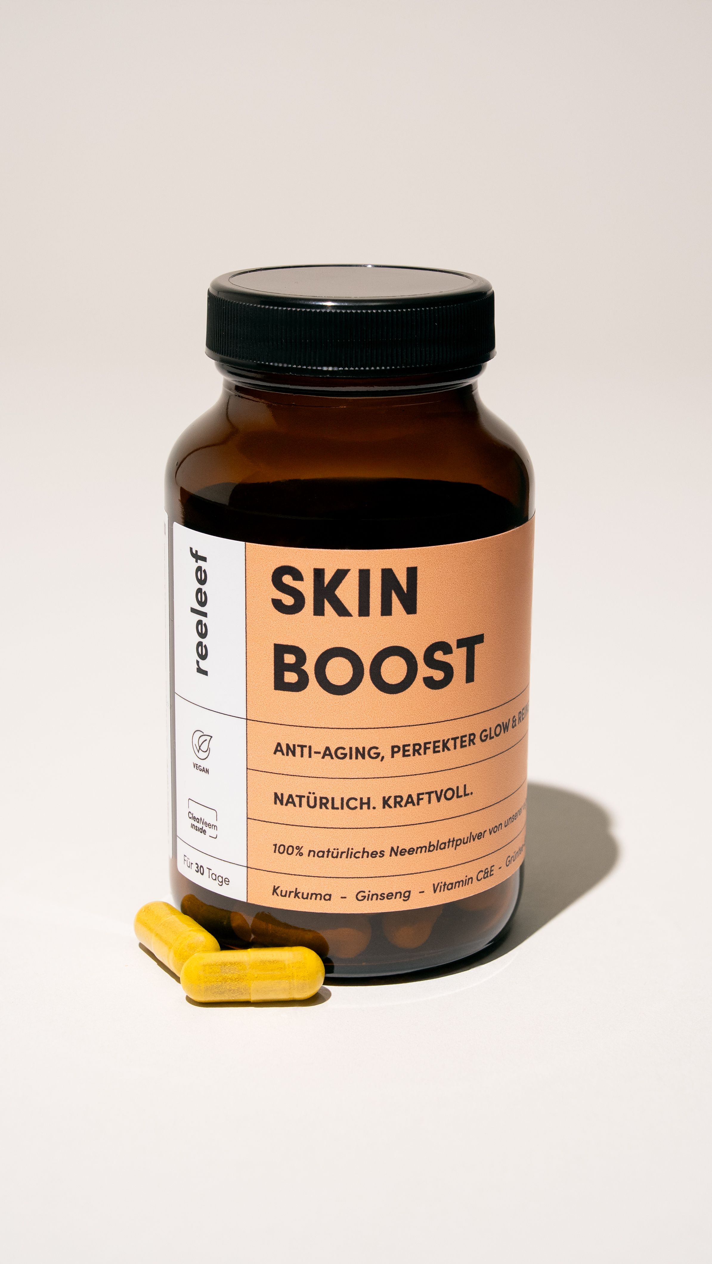 Braune Glasflasche mit Kapseln. Aufschrift SKIN BOOST. Vegan-Siegel. Kapseln liegen daneben.