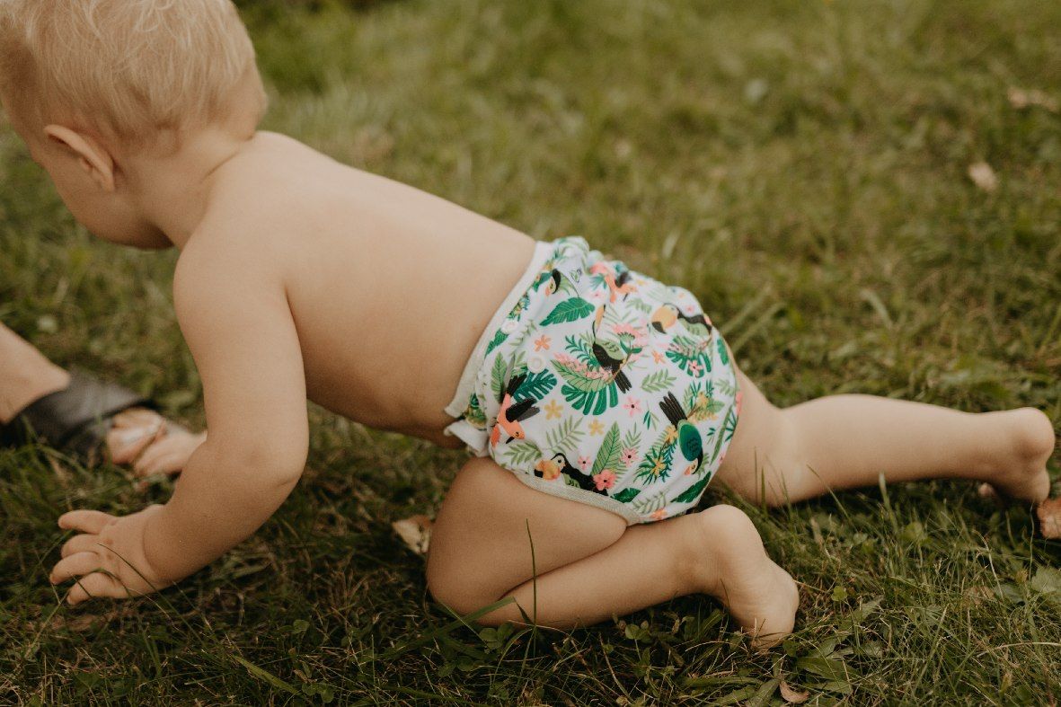 Baby krabbelt auf einer Wiese, trägt eine T-TOMI Schwimmwindel mit tropischem Tiermotiv.