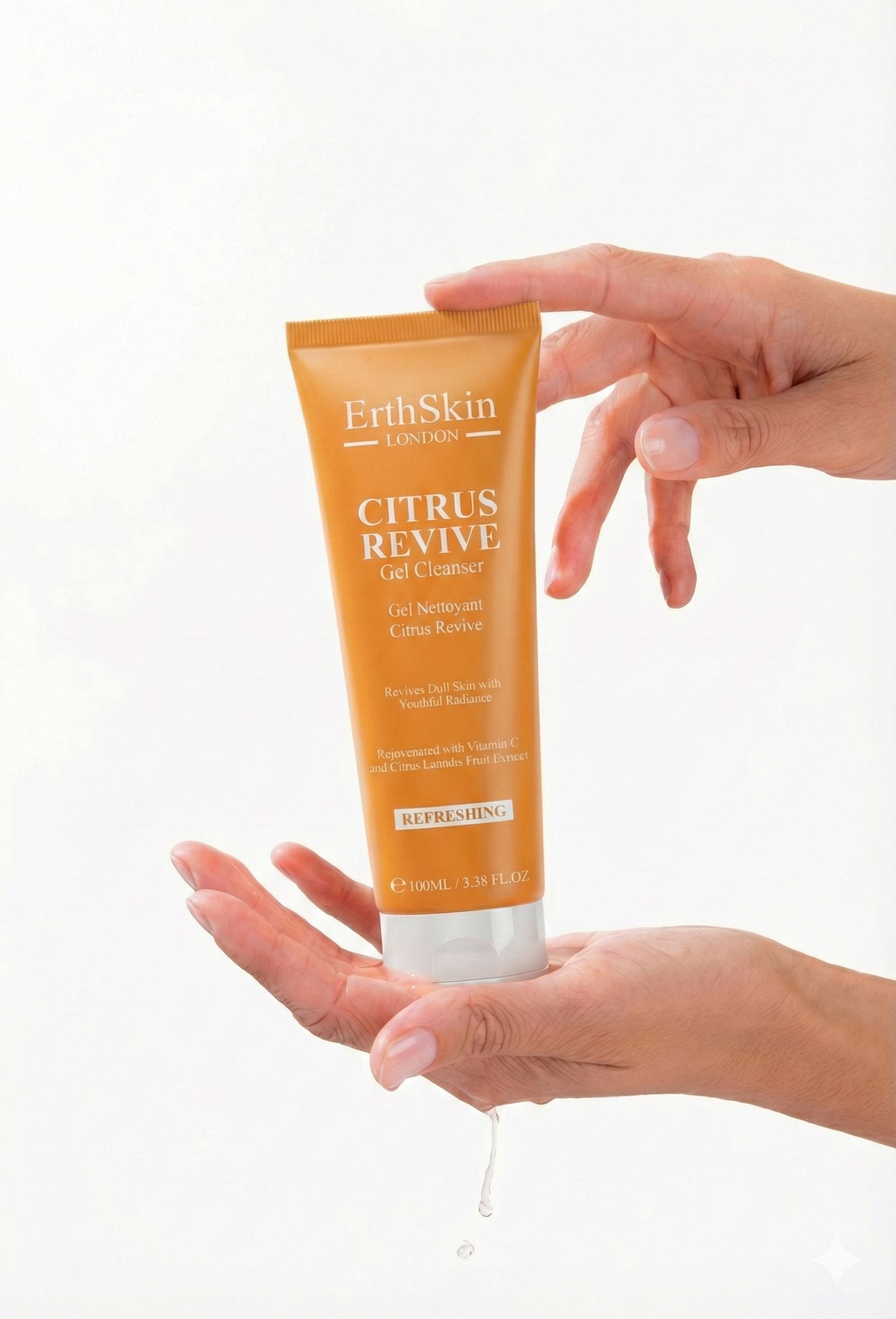 Hände halten eine orangefarbene Tube. Aufschrift: ErthSkin London CITRUS REVIVE Gel Cleanser. Tropfen Flüssigkeit.